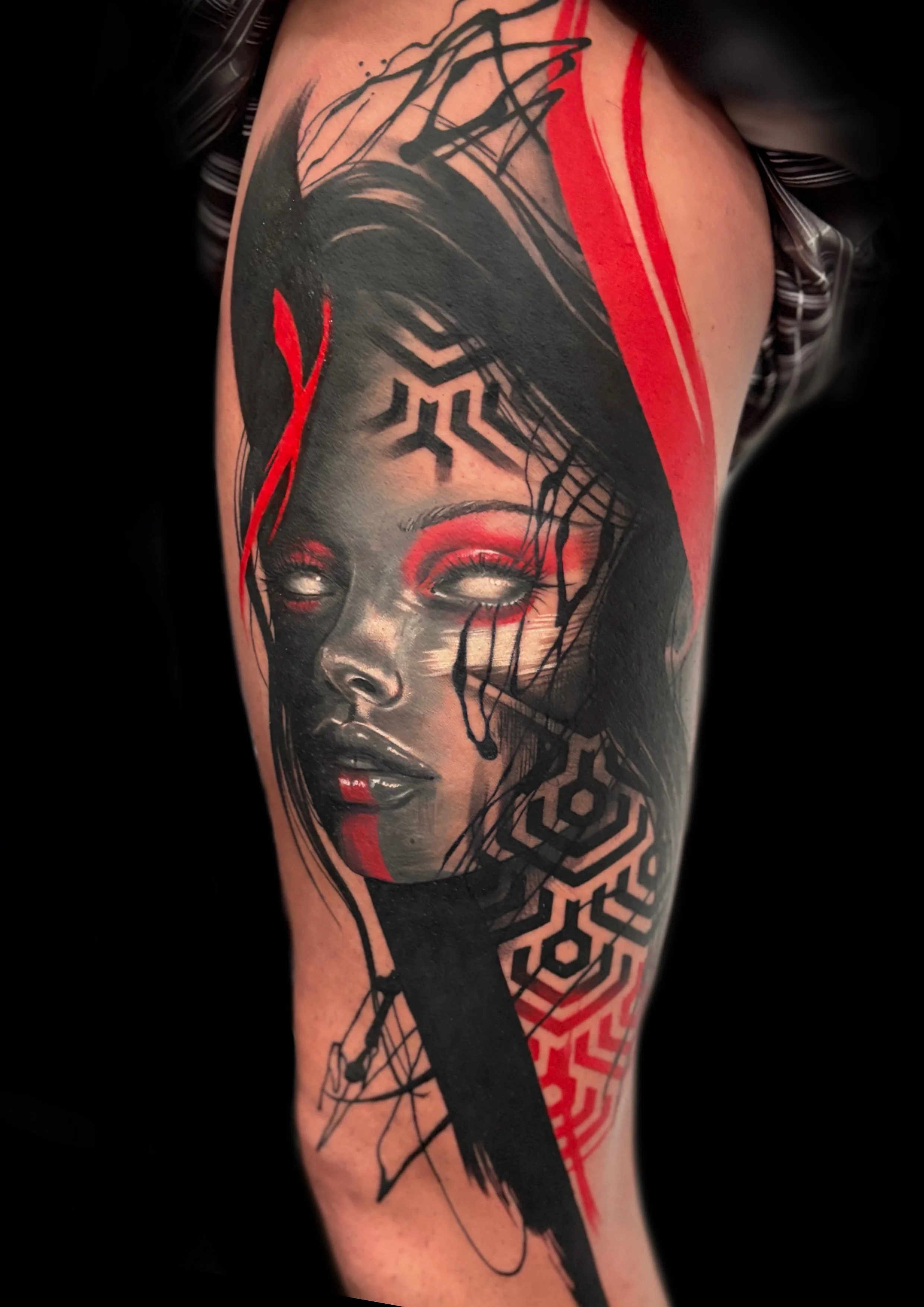 Tattoo of a woman's face with red makeup, black abstract lines, and geometric patterns on the arm.