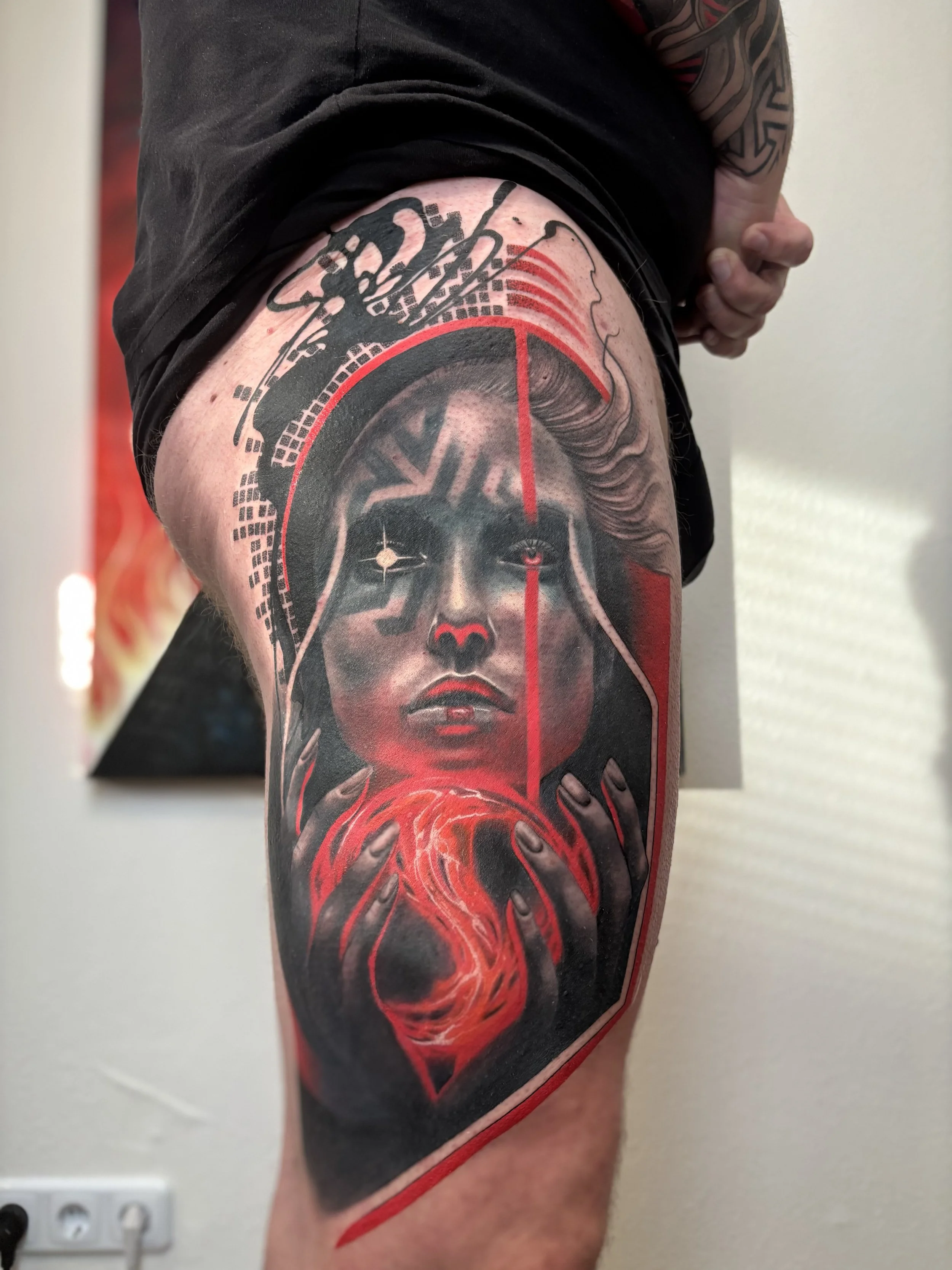 Tattoo of a woman's face with long hair, holding a glowing orb, surrounded by abstract red and black designs on a person's upper arm.