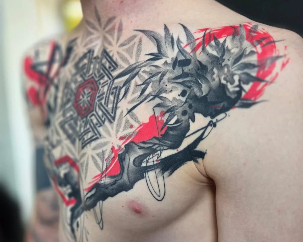 Close-up of a person's chest and shoulder showing a large, intricate tattoo featuring a face of a woman, geometric patterns, and abstract elements in black, gray, and red ink.