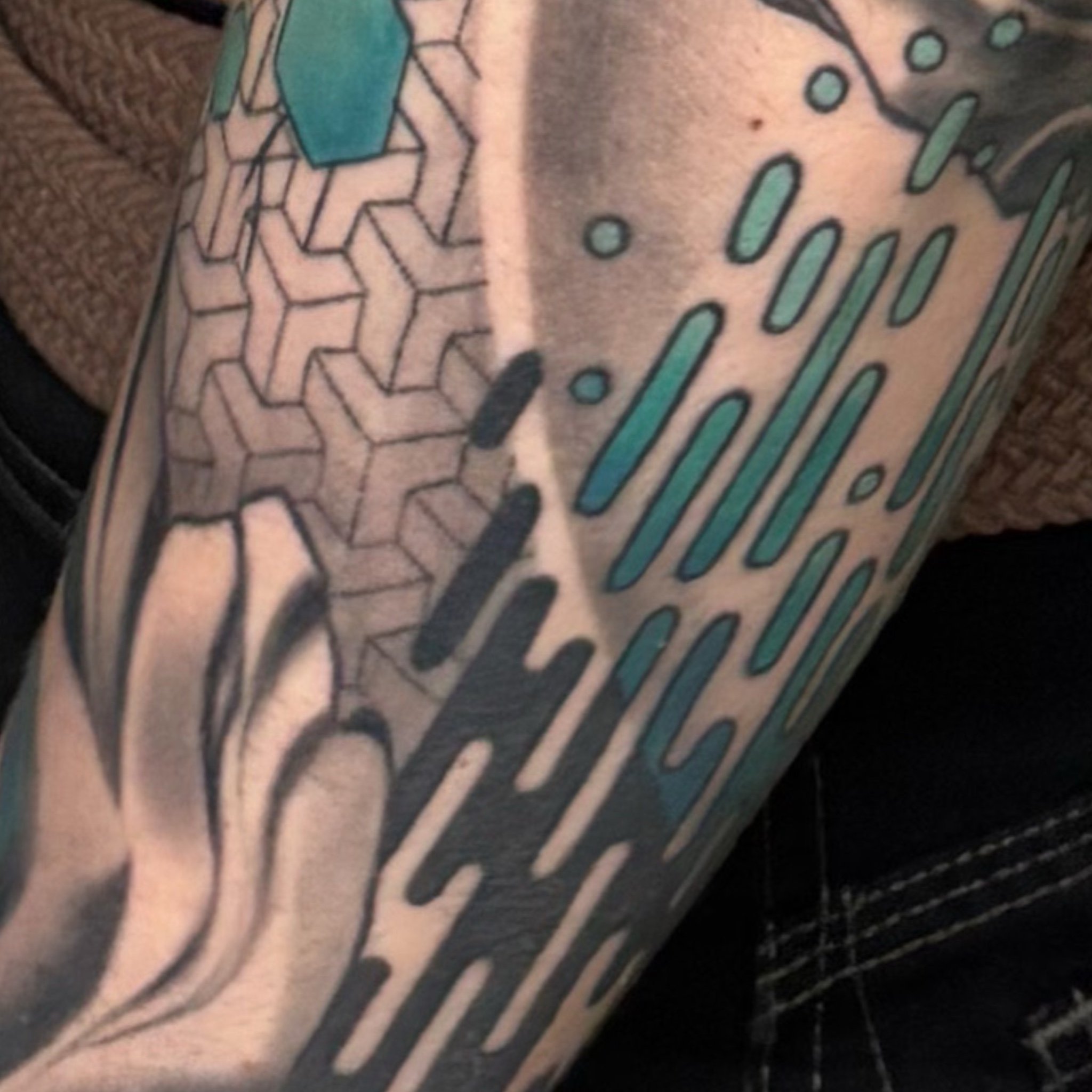 Close-up view of a tattoo on skin, featuring geometric patterns and lines in black ink with teal accents.