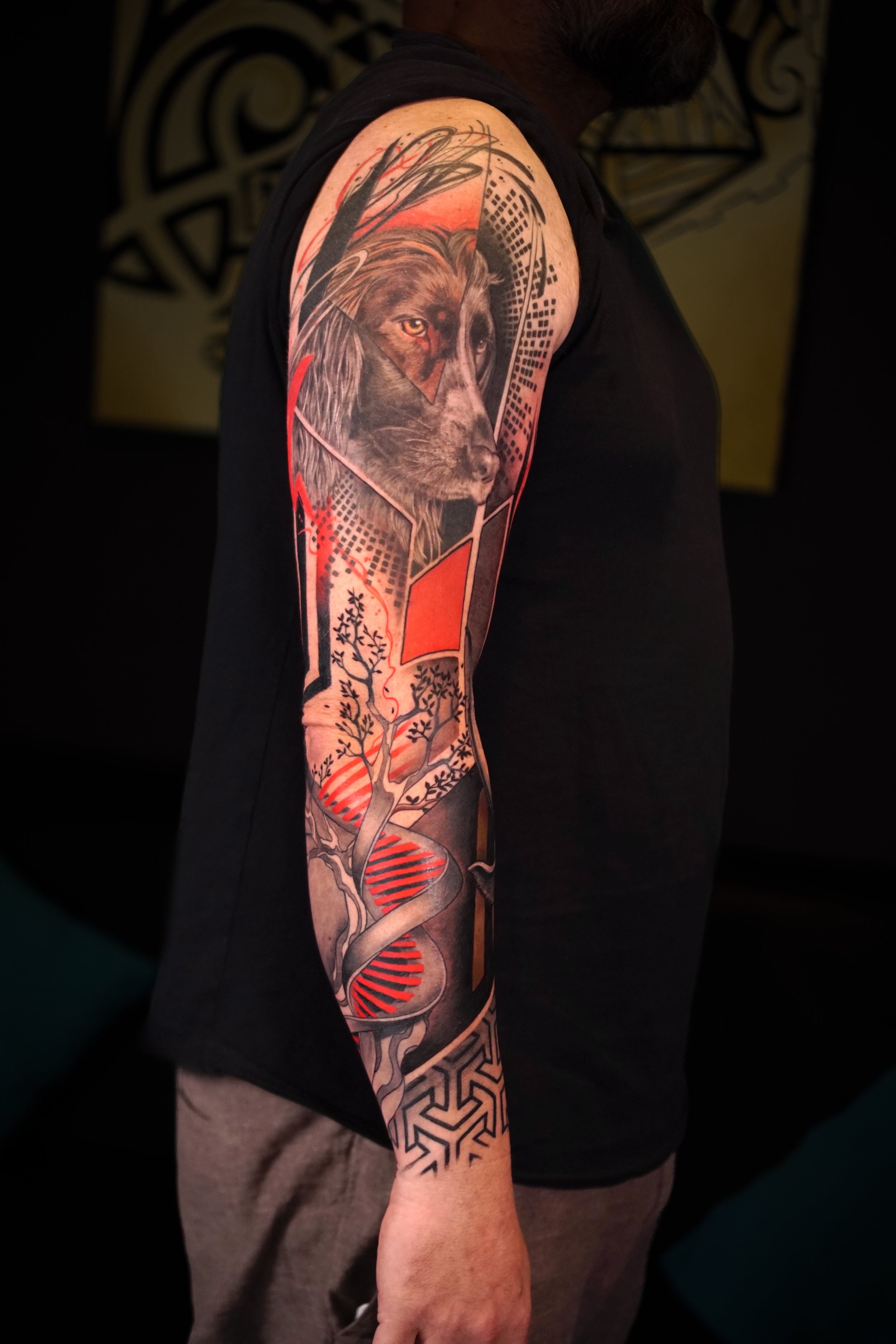 Tattoo of a lion's face on a person's upper arm with abstract geometric and natural designs, including a DNA helix on the forearm.