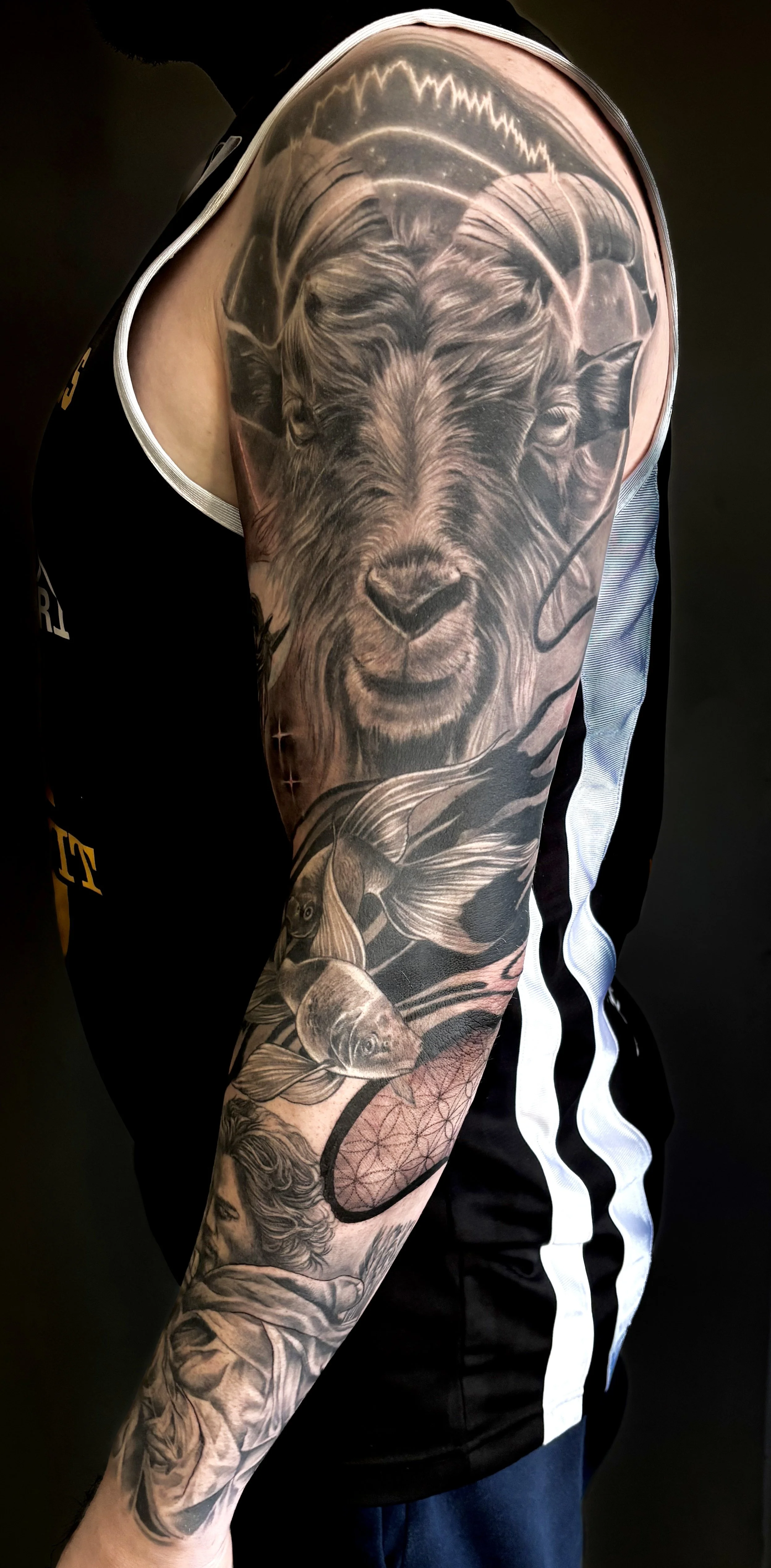 Black and gray arm tattoo featuring a bear's face, a fish, and an abstract design on a person's arm, with a black shirt with white trim.