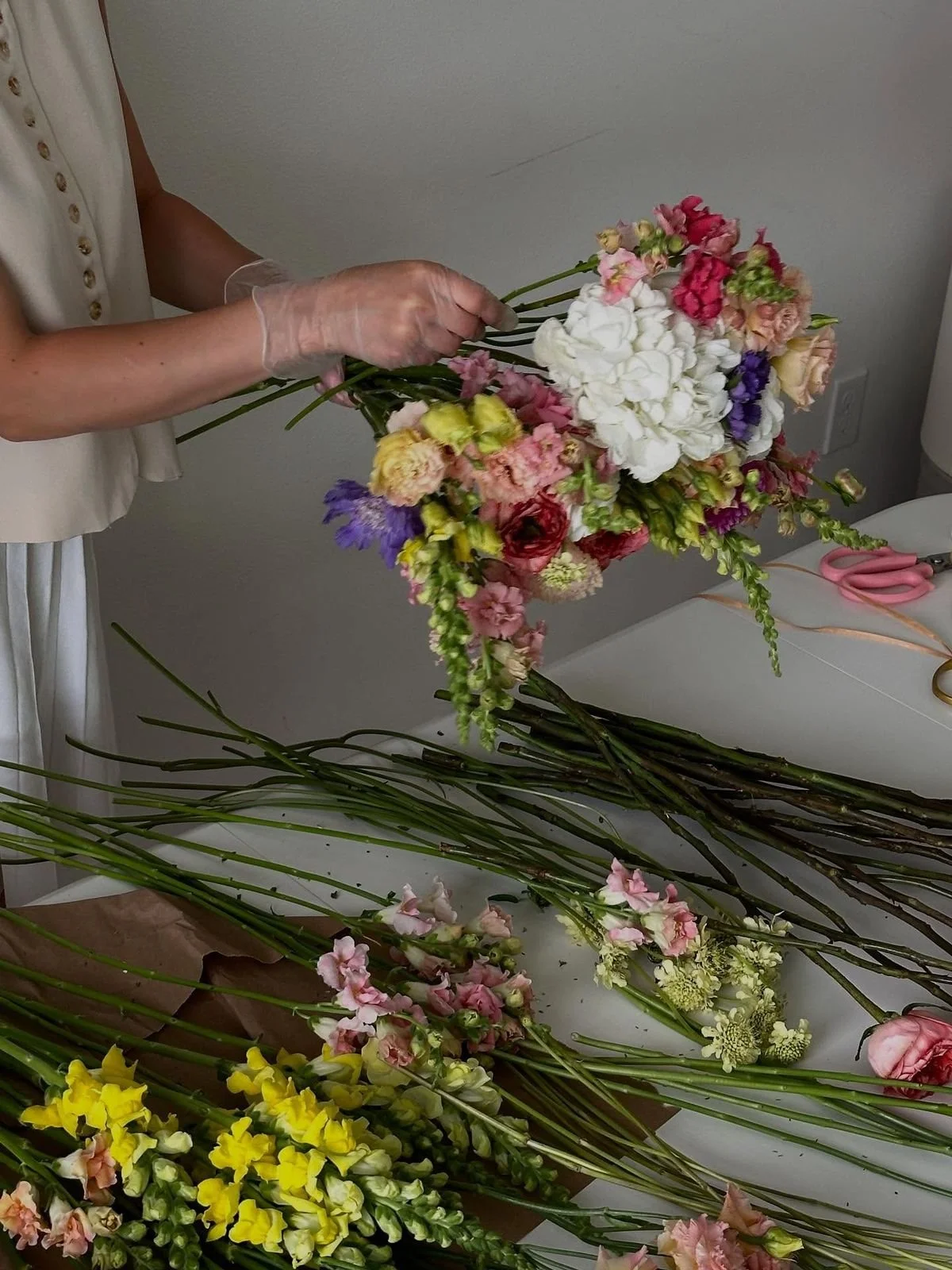 Person arranging a colorful bouquet of flowers on a table, with scissors and flower stems nearby.
