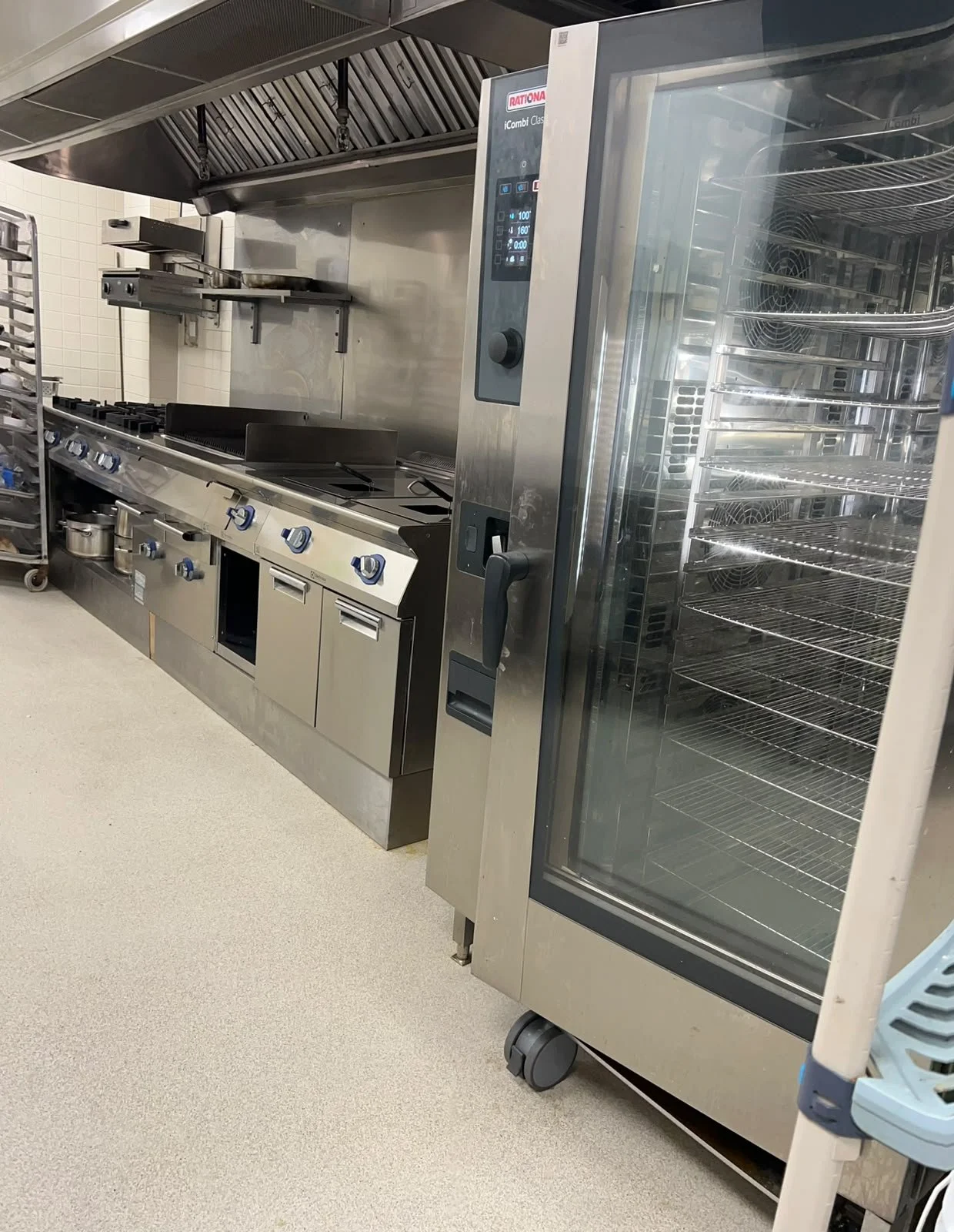 Cocina industrial con estufa, horno y una nevera de acero inoxidable en un entorno de cocina profesional.