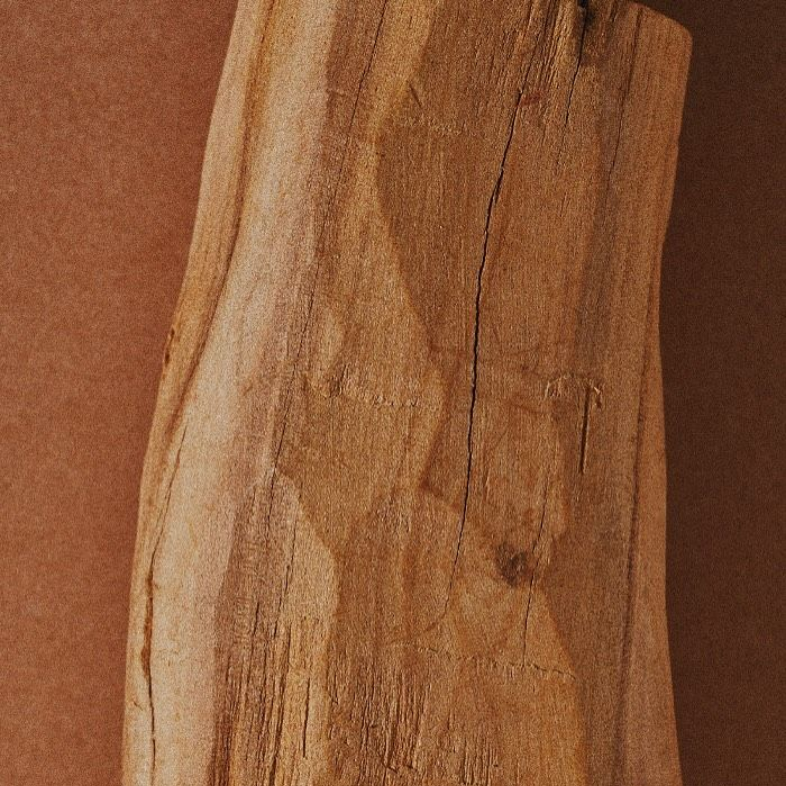 Close-up of a wooden surface with visible grain and cracks, showing warm brown tones.