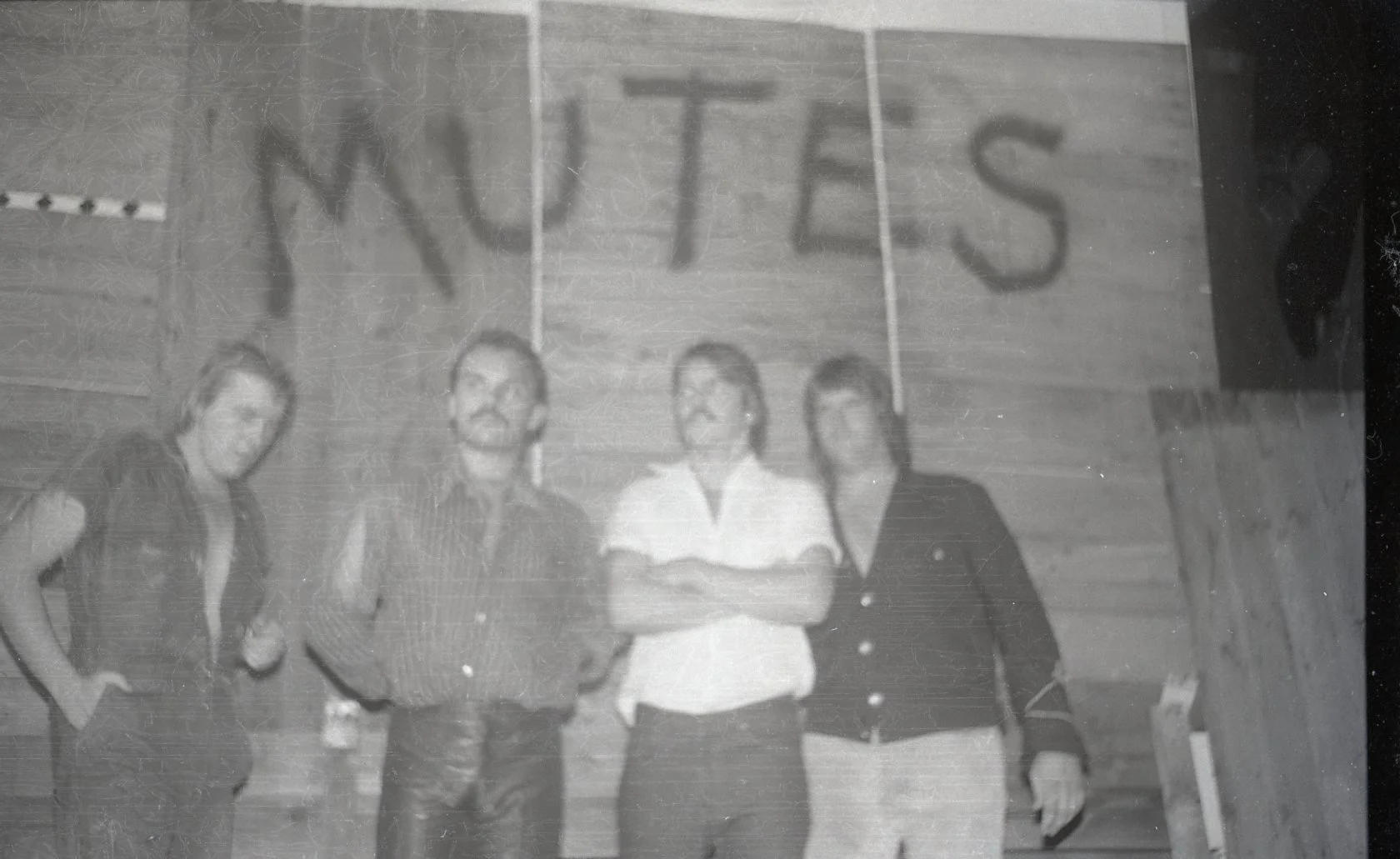 Four people standing in front of a wooden wall with a sign that says "NUTS" in a gymnasium or auditorium setting.
