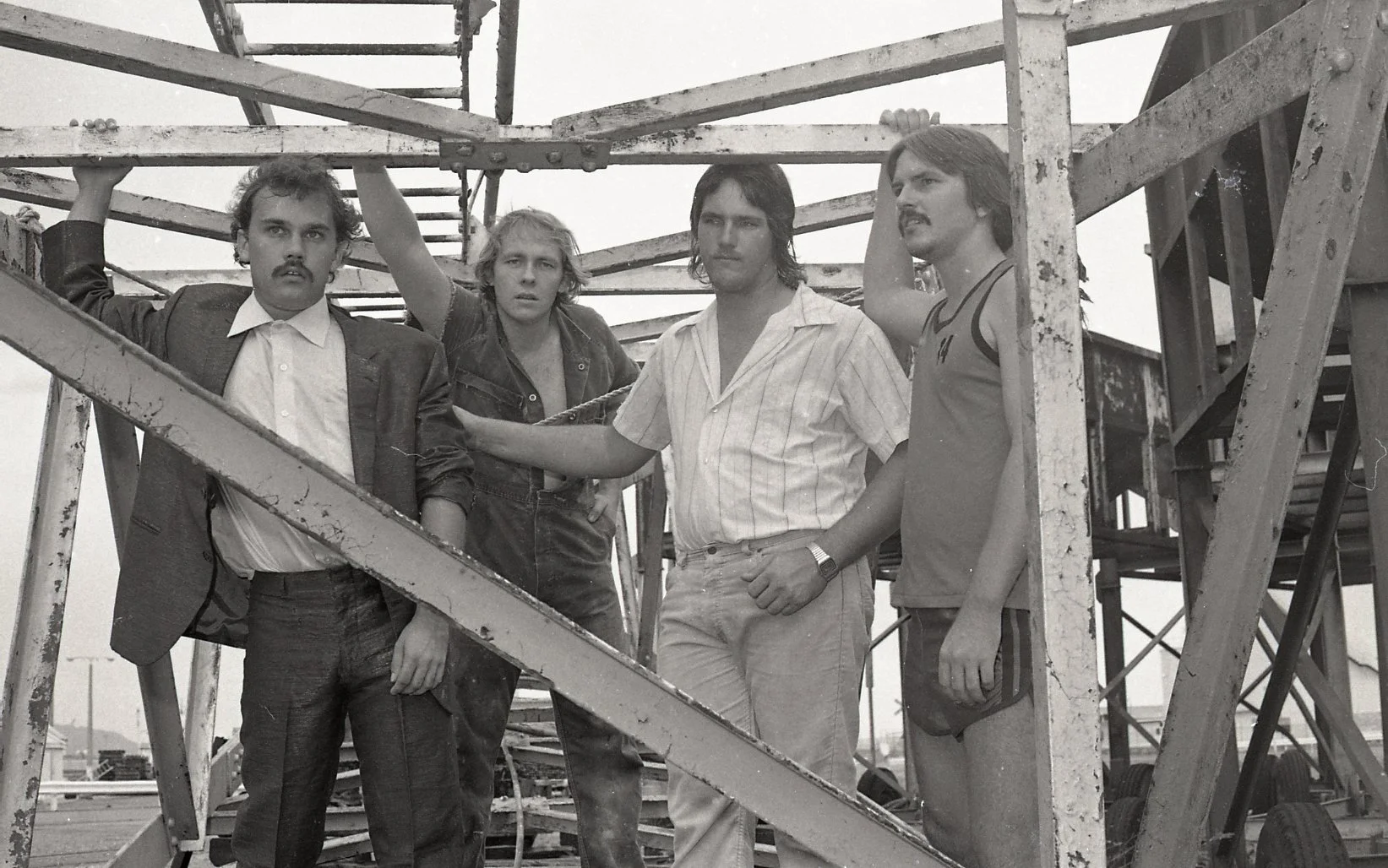 Five men standing on a construction site, posing for a photo with scaffolding around them. The image is in black and white.