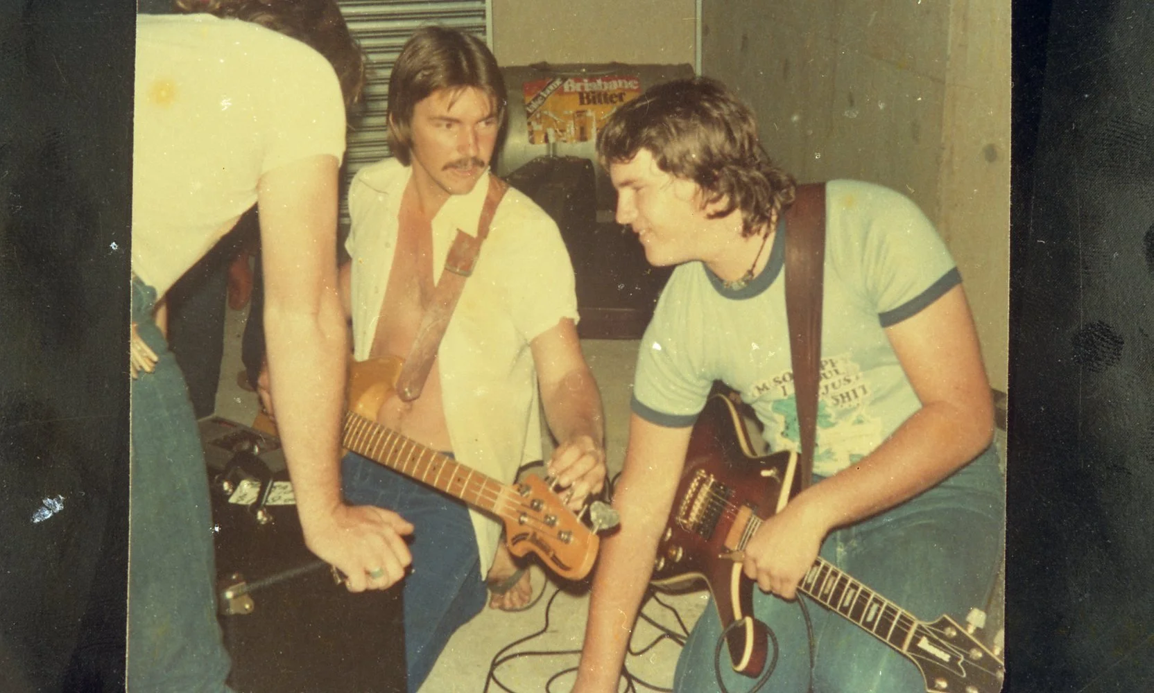 Two young men with guitars in a room, one with a strap over his shoulder, the other holding his guitar, appearing to be preparing to play music.