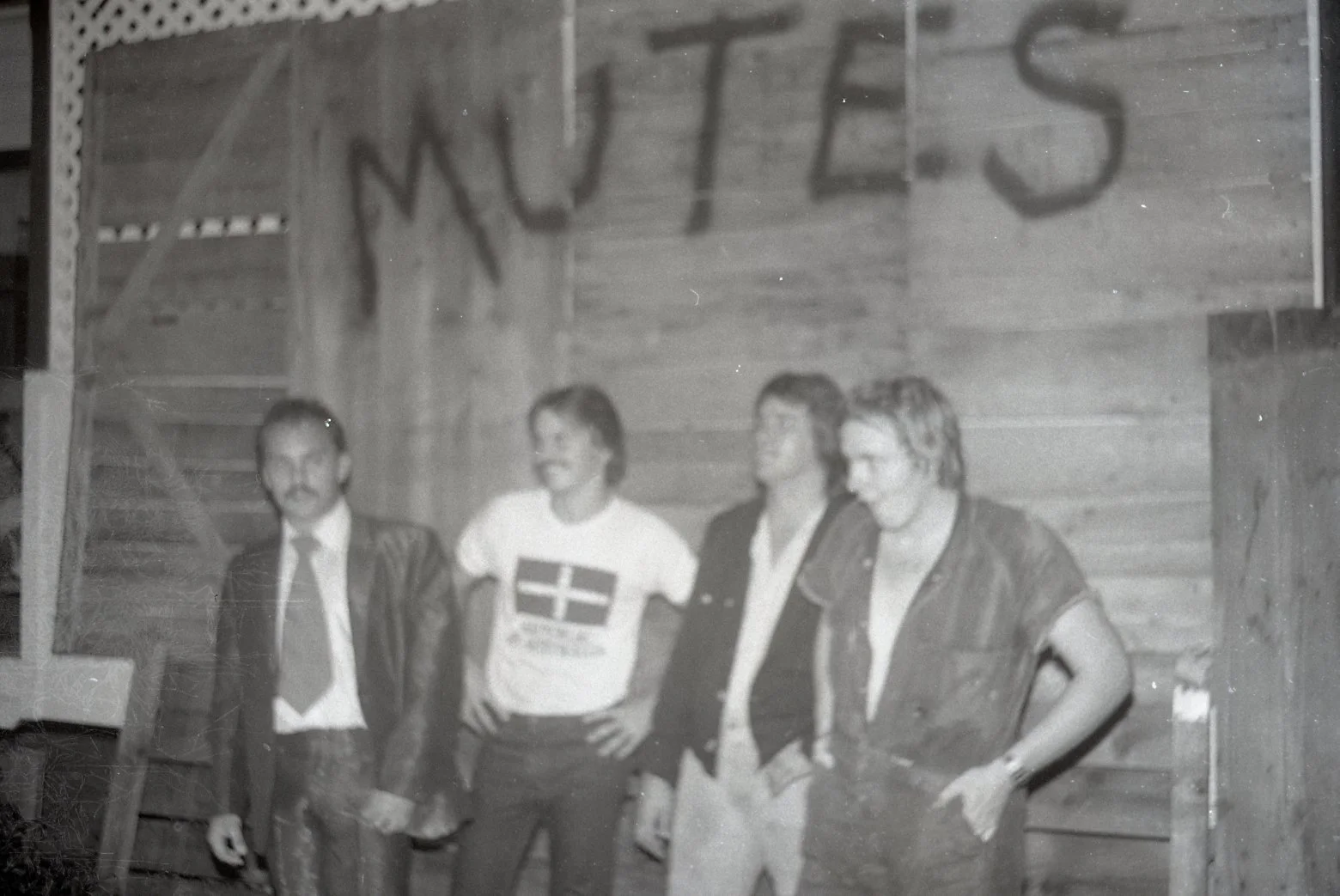 Black-and-white photo of four people standing inside a wooden building with a sign above them that says 'MOTELS'.