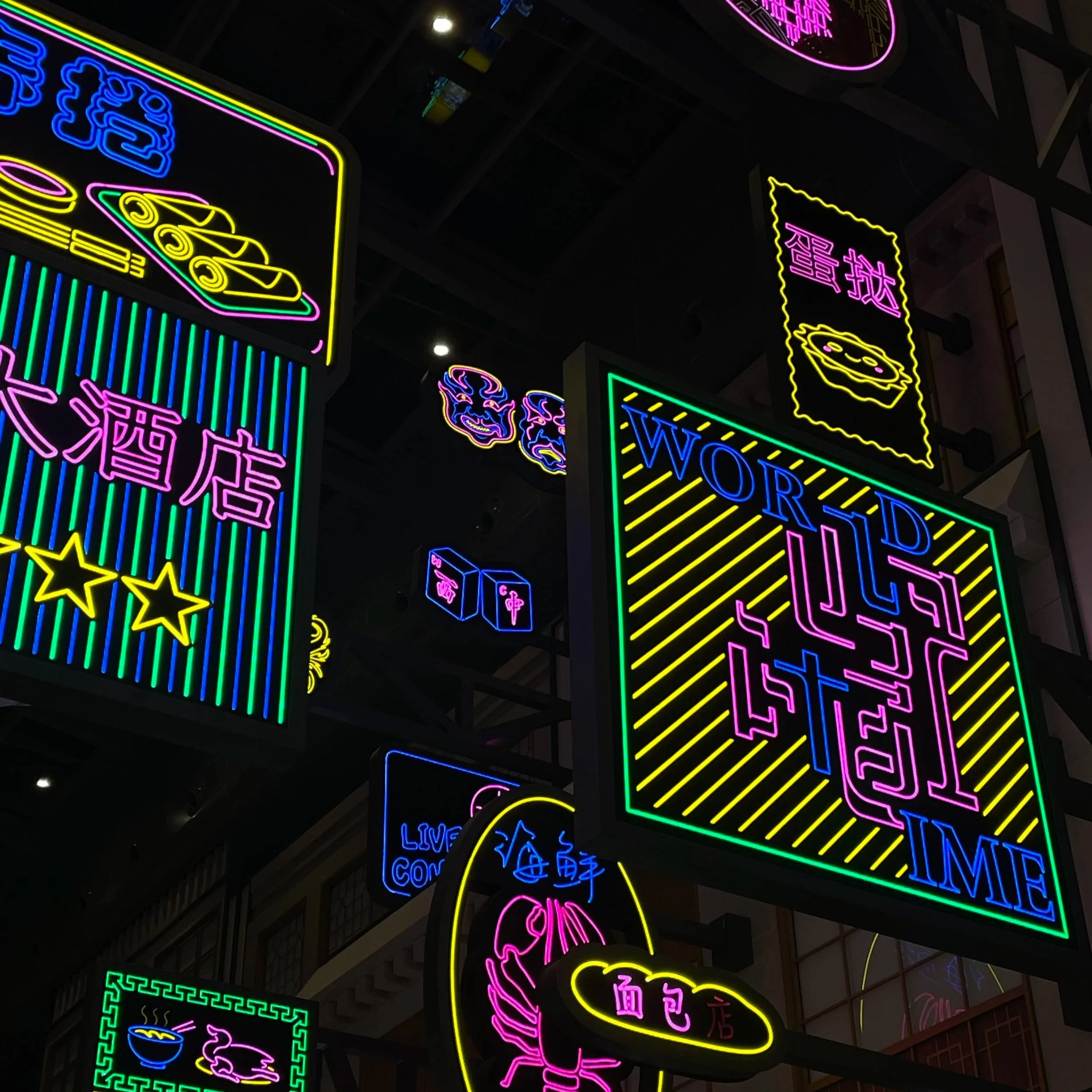 Neon signs in Chinese and English advertising various food and drink items, including noodles, dumplings, and beverages, with bright vibrant colors on a dark background.