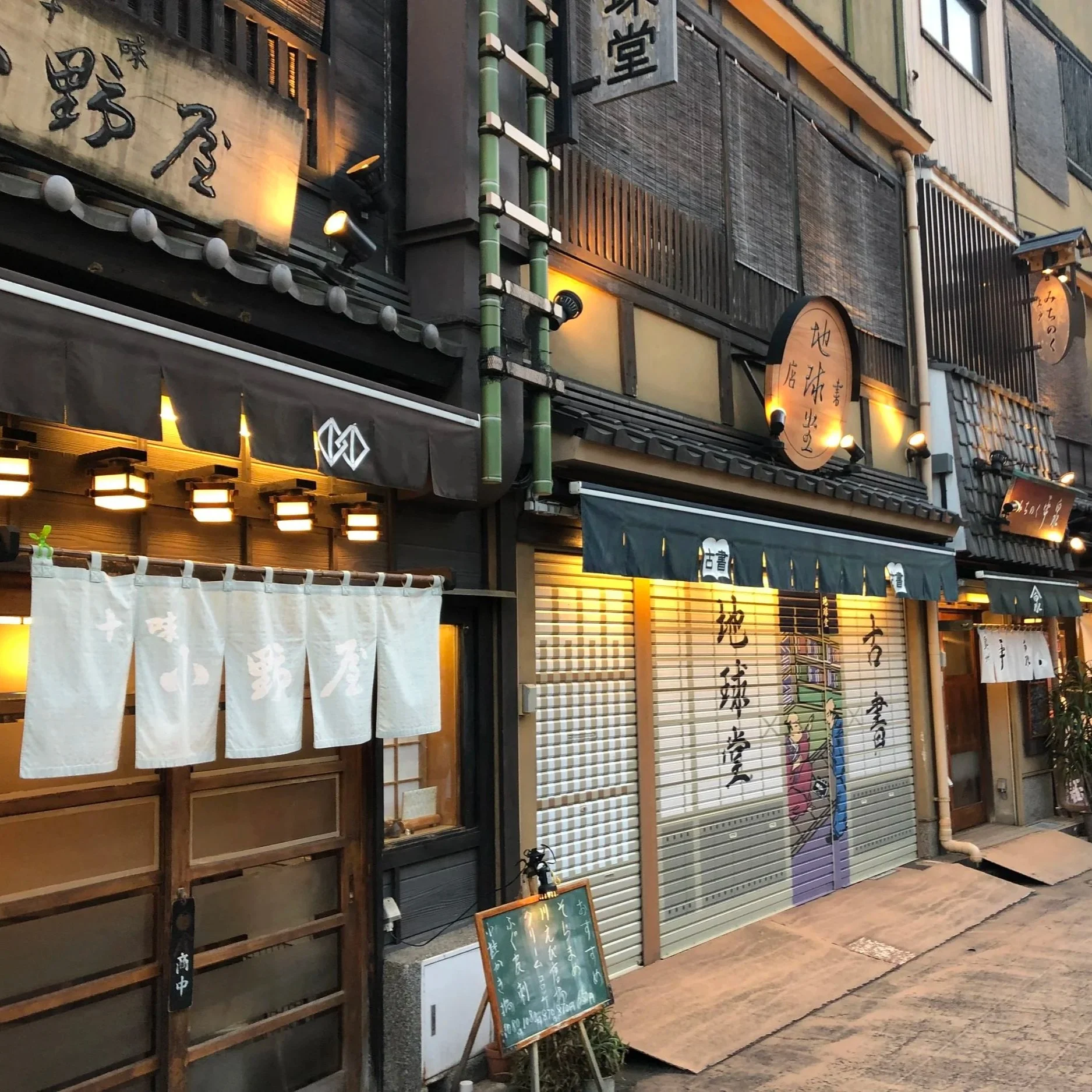 Facade of a Japanese restaurant with traditional wooden signs and paper lanterns, exterior decoration with bamboo and hanging fabric banners with Japanese writing.