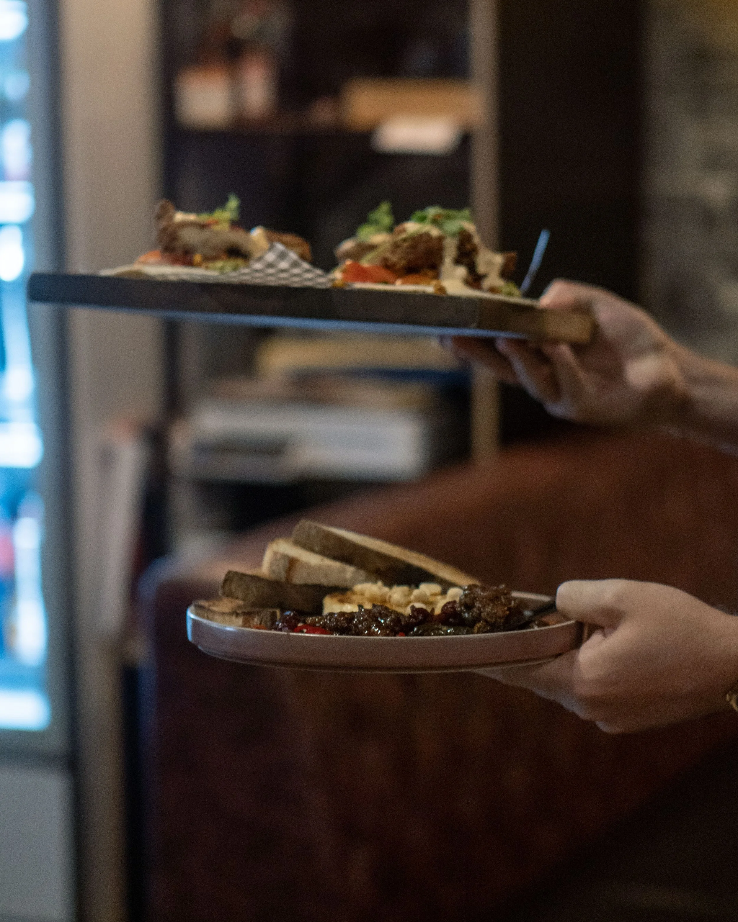 A person holding a plate of food in a restaurant, with background shelves and a blurred interior.