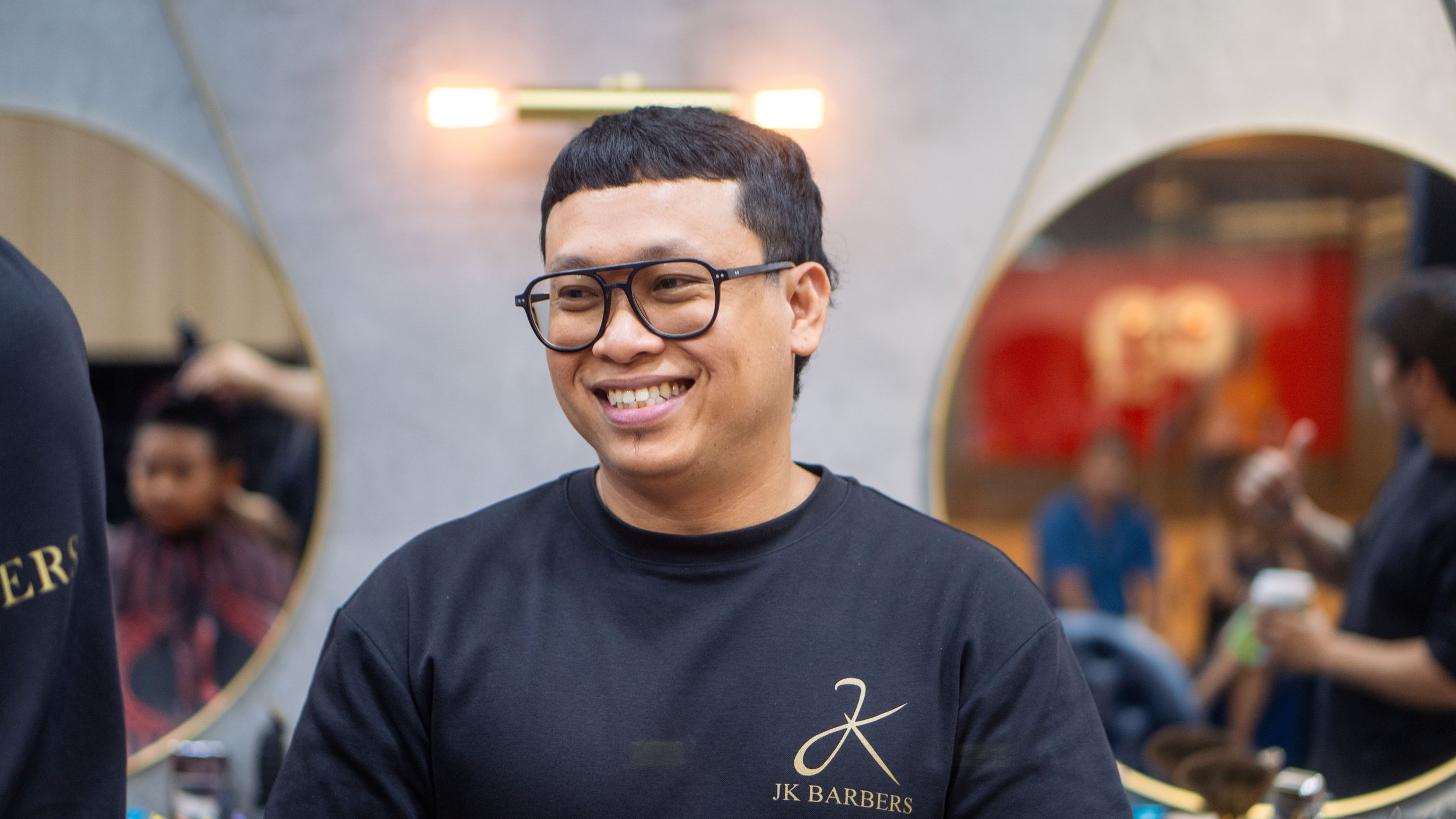 Smiling man with glasses and black t-shirt in barbershop.
