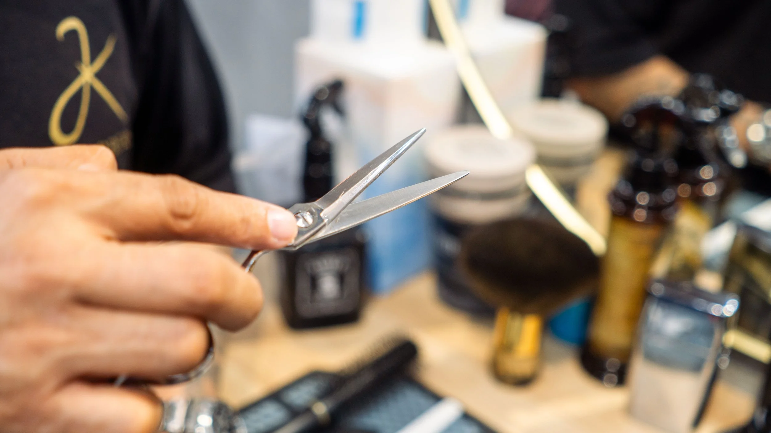 Close-up of a person's hand holding a pair of scissors in a workshop or salon setting.