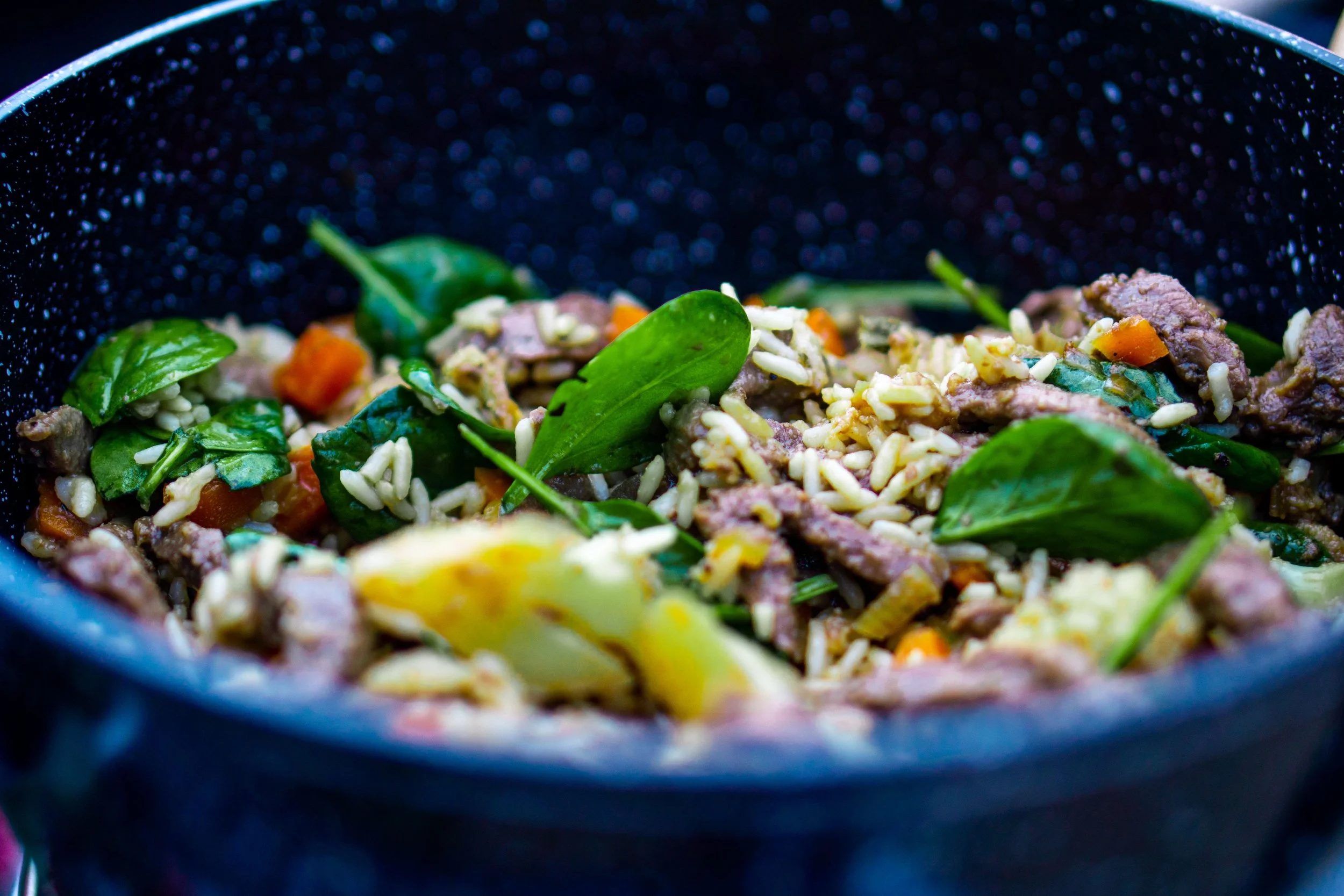 Close-up of a sautéed dish with greens, rice, and chopped vegetables in a black skillet.