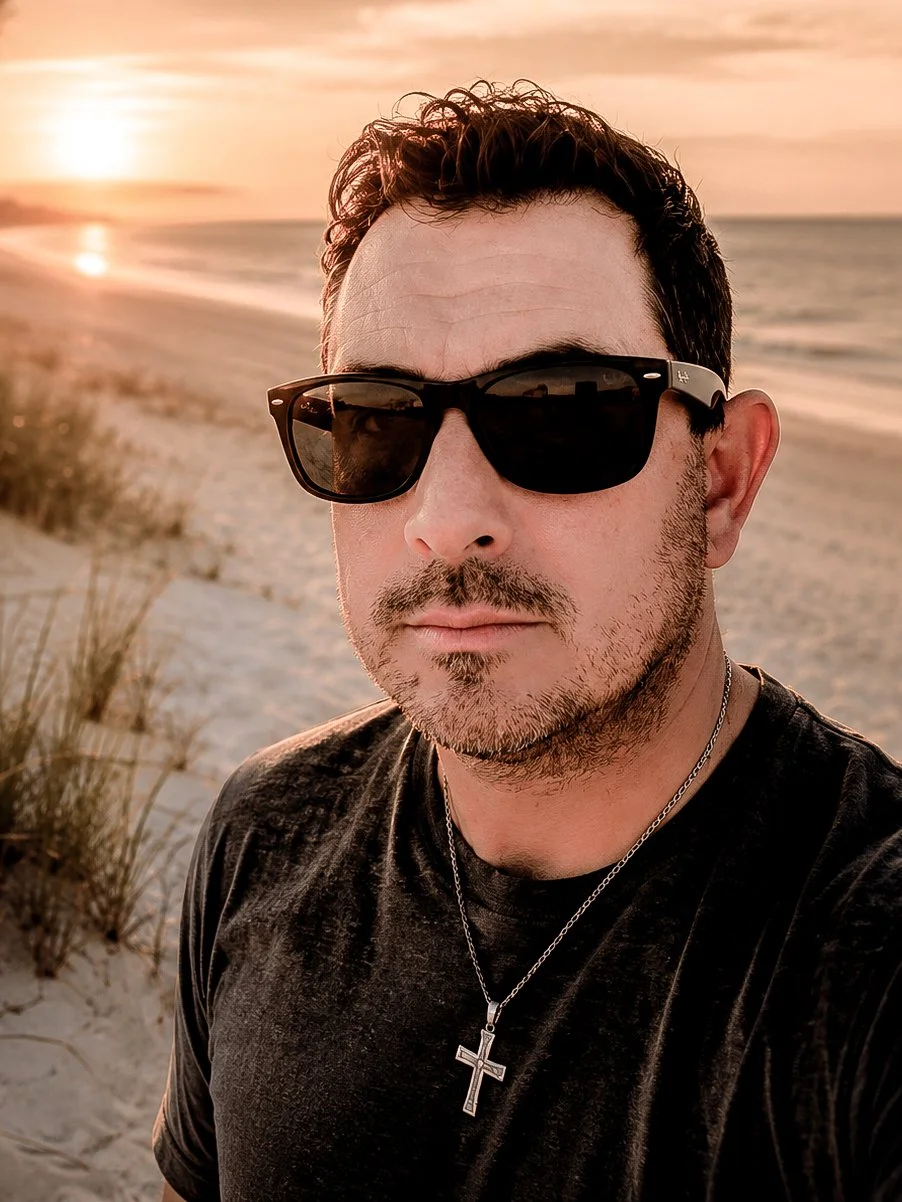 Mike, co-founder of River Branch Adventure Co, standing on a quiet beach at sunset with warm coastal light reflecting across the shoreline.
