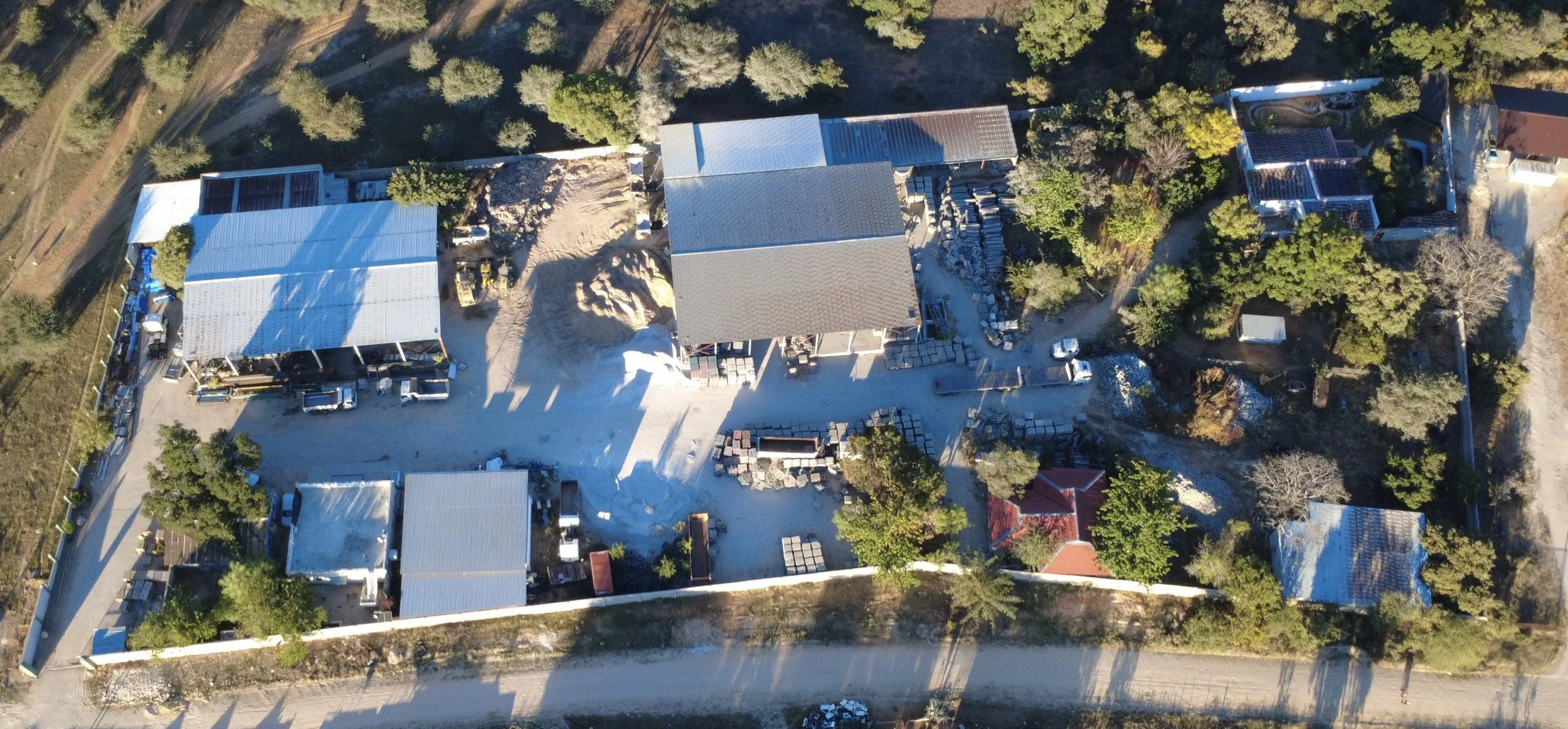 An aerial view of a construction site with multiple buildings in progress, surrounded by trees and parked vehicles.