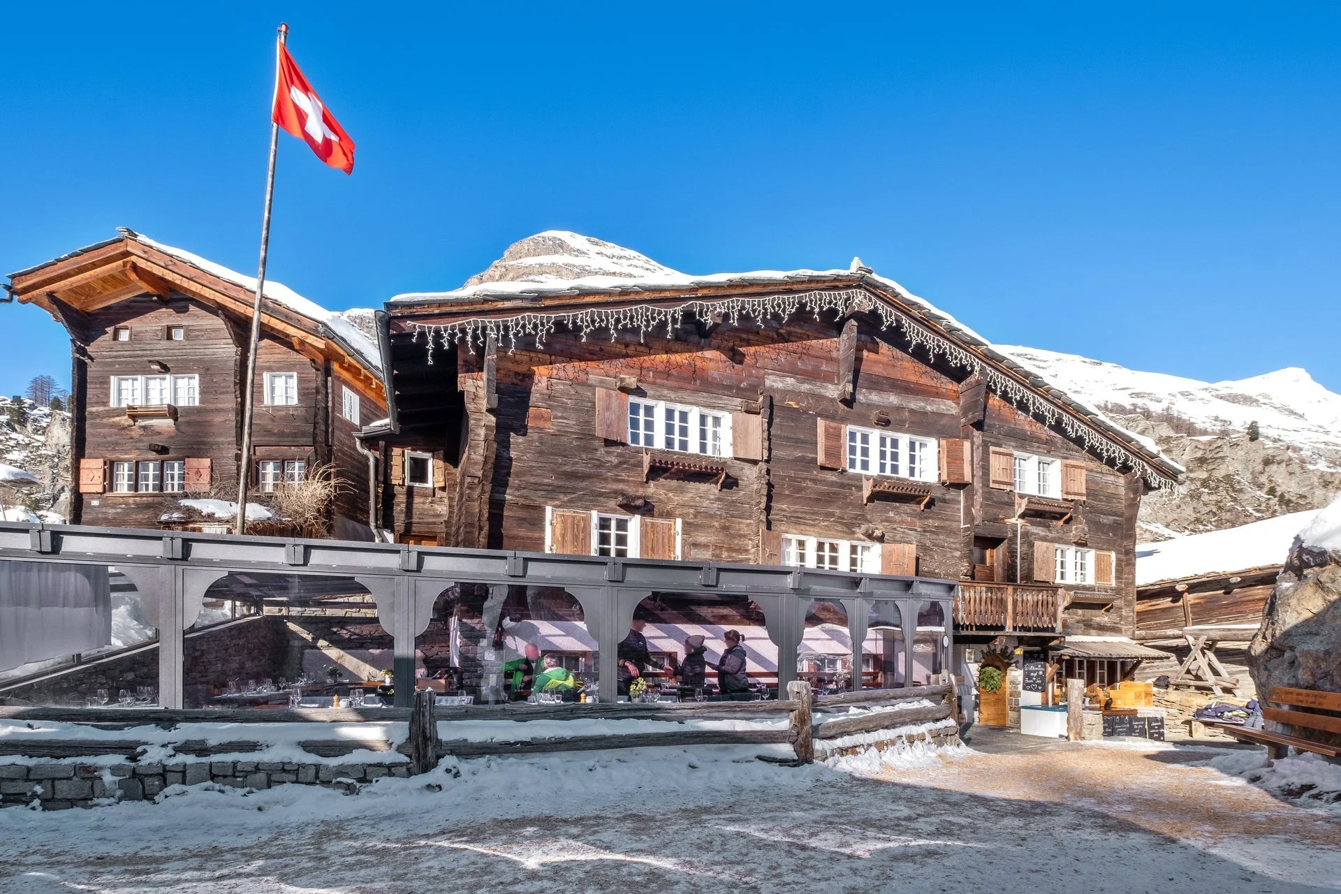 Holzhaus in den Bergen mit Schweizerfahne, Schneefall, Winter, Terrassen mit Menschen