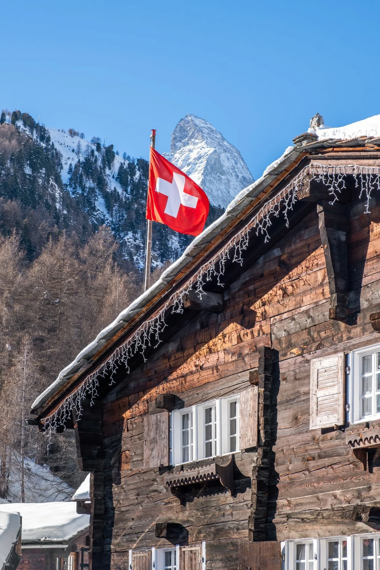 Schneebedecktes Chalet in den Schweizer Alpen mit Schweizer Flagge, im Hintergrund Berge und blauer Himmel.
