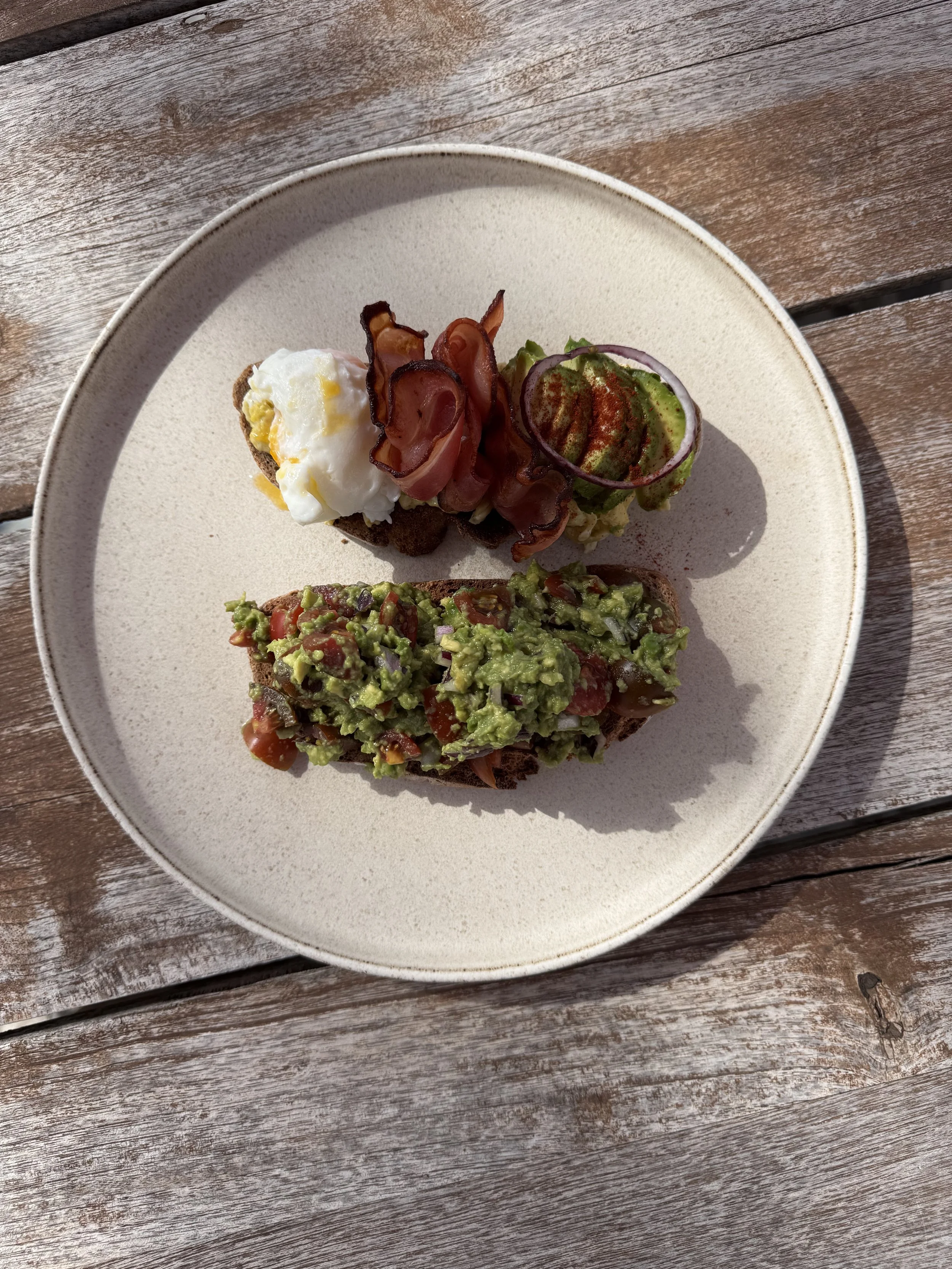 Open-faced sandwich with mashed avocado, chopped tomatoes, red onion, topped with paprika, on rustic wooden table.