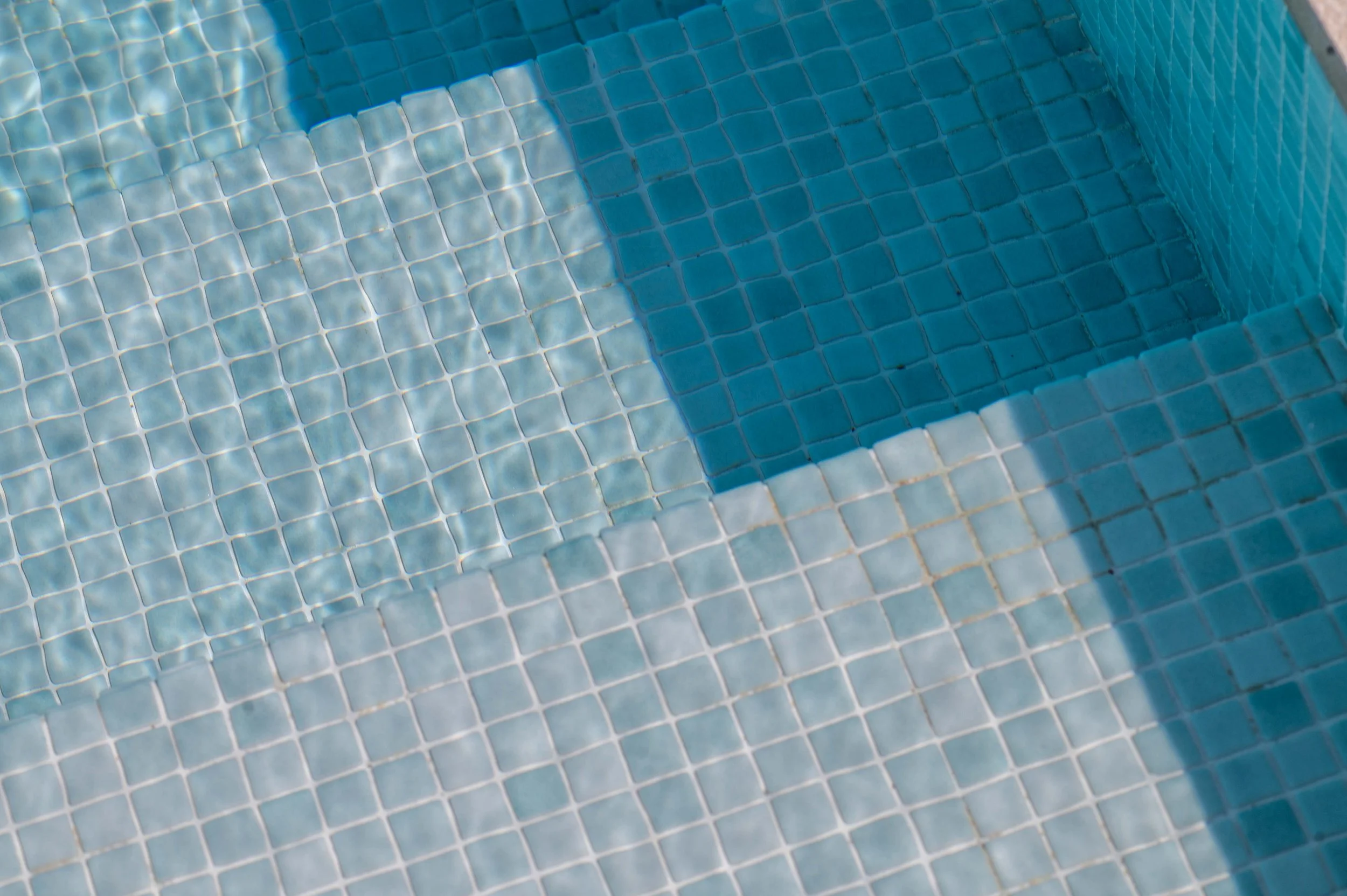 Close-up of a swimming pool with light blue tiles and water surface reflecting sunlight.