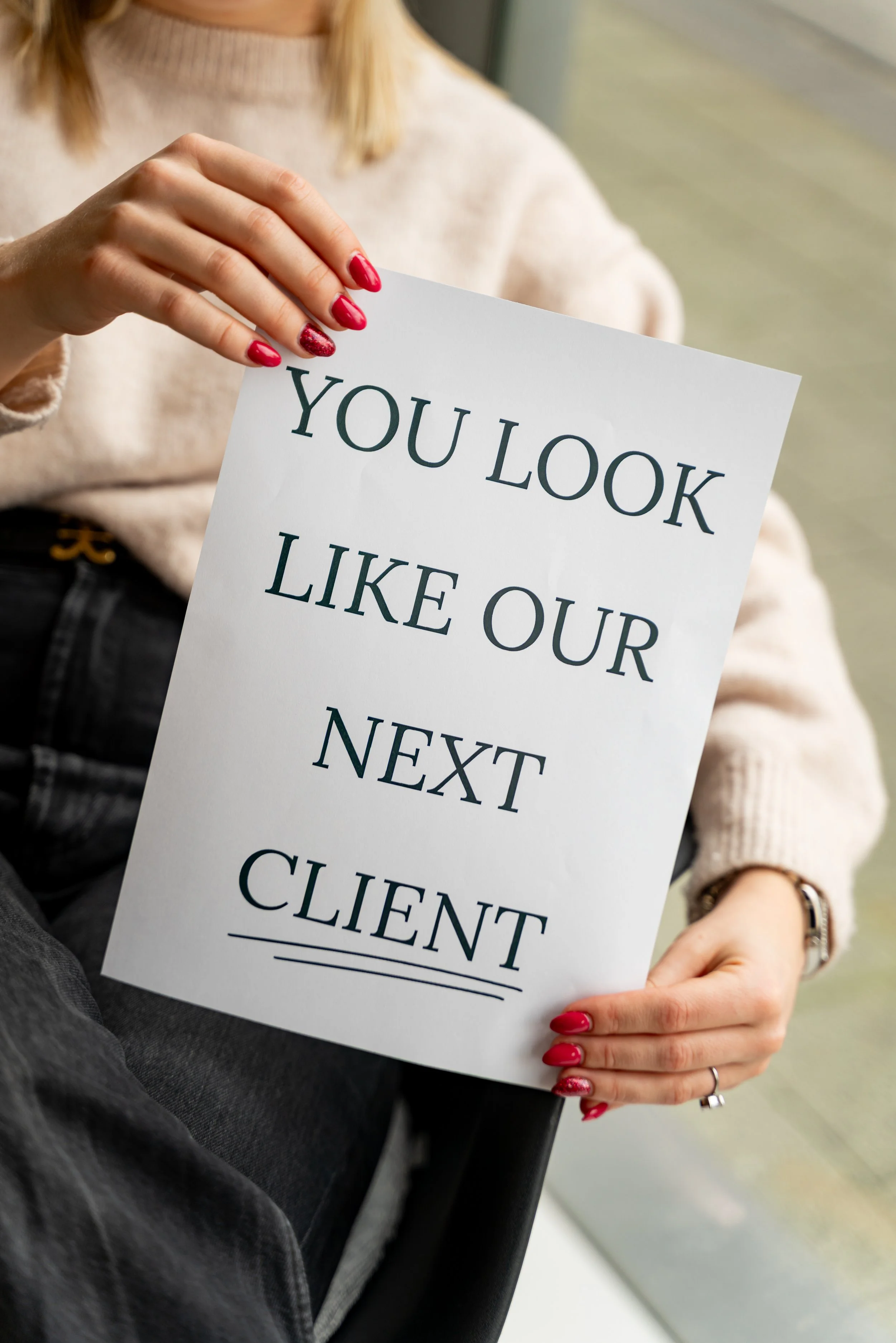 Een persoon houdt een wit bord met de tekst 'YOU LOOK LIKE OUR NEXT CLIENT'.