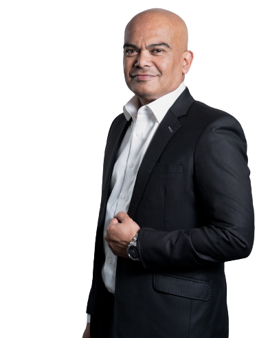 A confident man in a black suit with a white shirt standing against a black background.