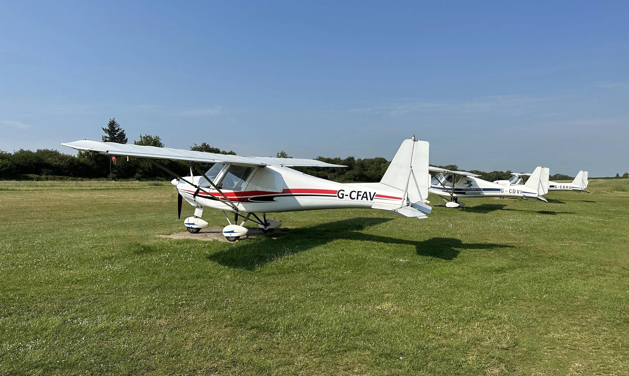 Three small propeller airplanes parked on a grassy field under a clear blue sky.
