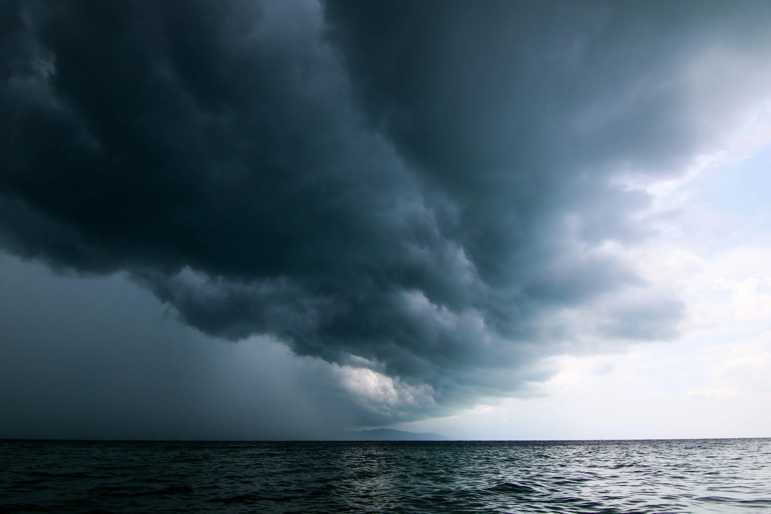 Dark, stormy clouds over a body of water, with a faint outline of land in the distance.