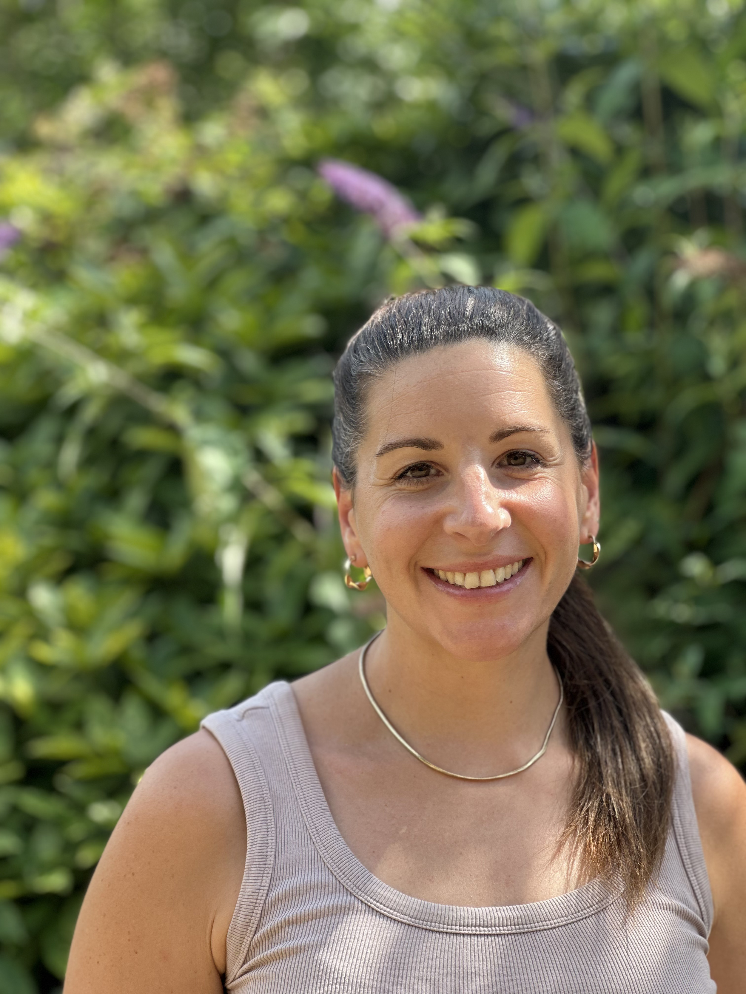 Natalie stands outdoors in a sunny garden, smiling to the camera.