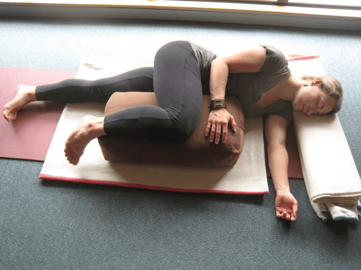Woman practicing a restorative yoga pose lying on a bolster and mat.