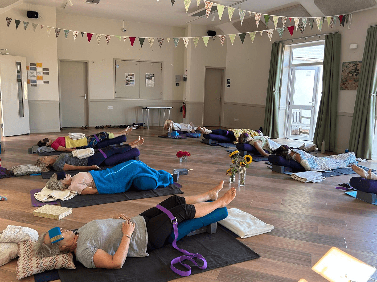 Group yoga class practicing supported reclining poses on mats in a decorated studio