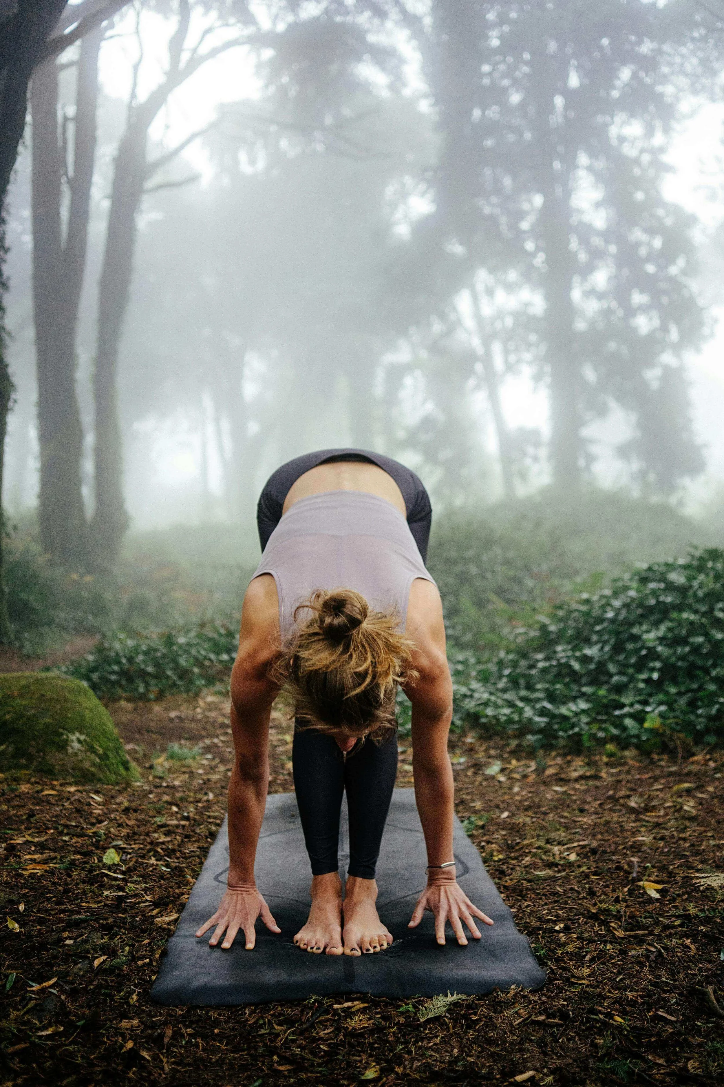 Woman practicing yoga on a mat outdoors in a sunlit forest