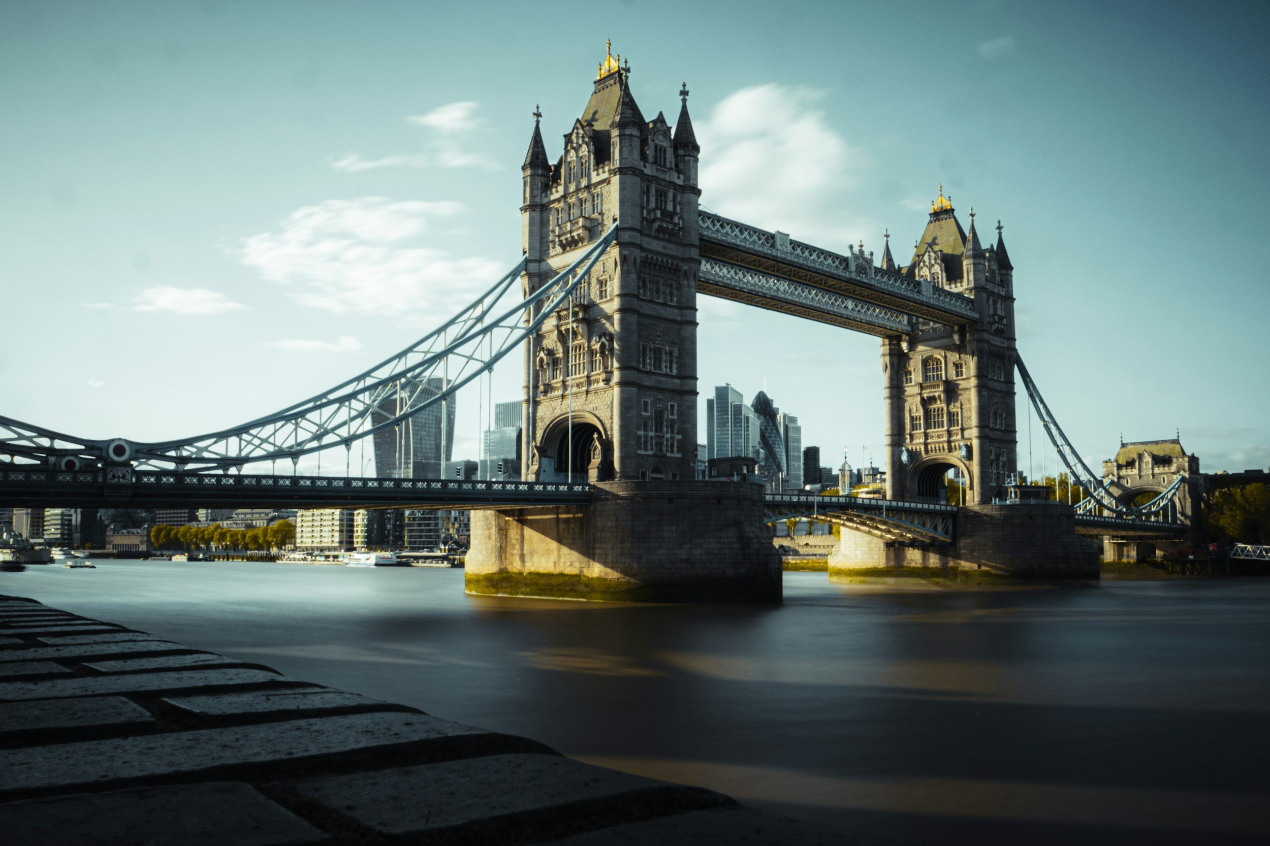 The Tower Bridge over the River Thames in London with modern skyscrapers in the background, during daytime.