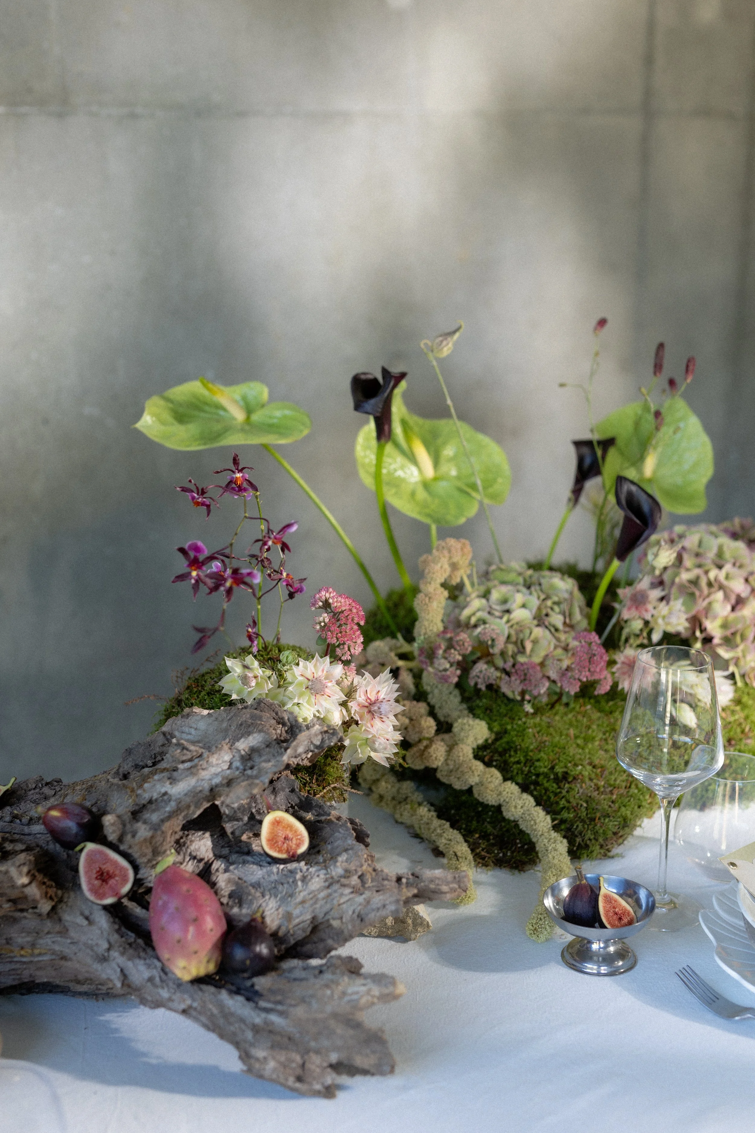 Table de buffet avec des fleurs, des figues coupées, des figues entières, et un verre à vin vide. Décor de fête élégante avec une disposition soignée.