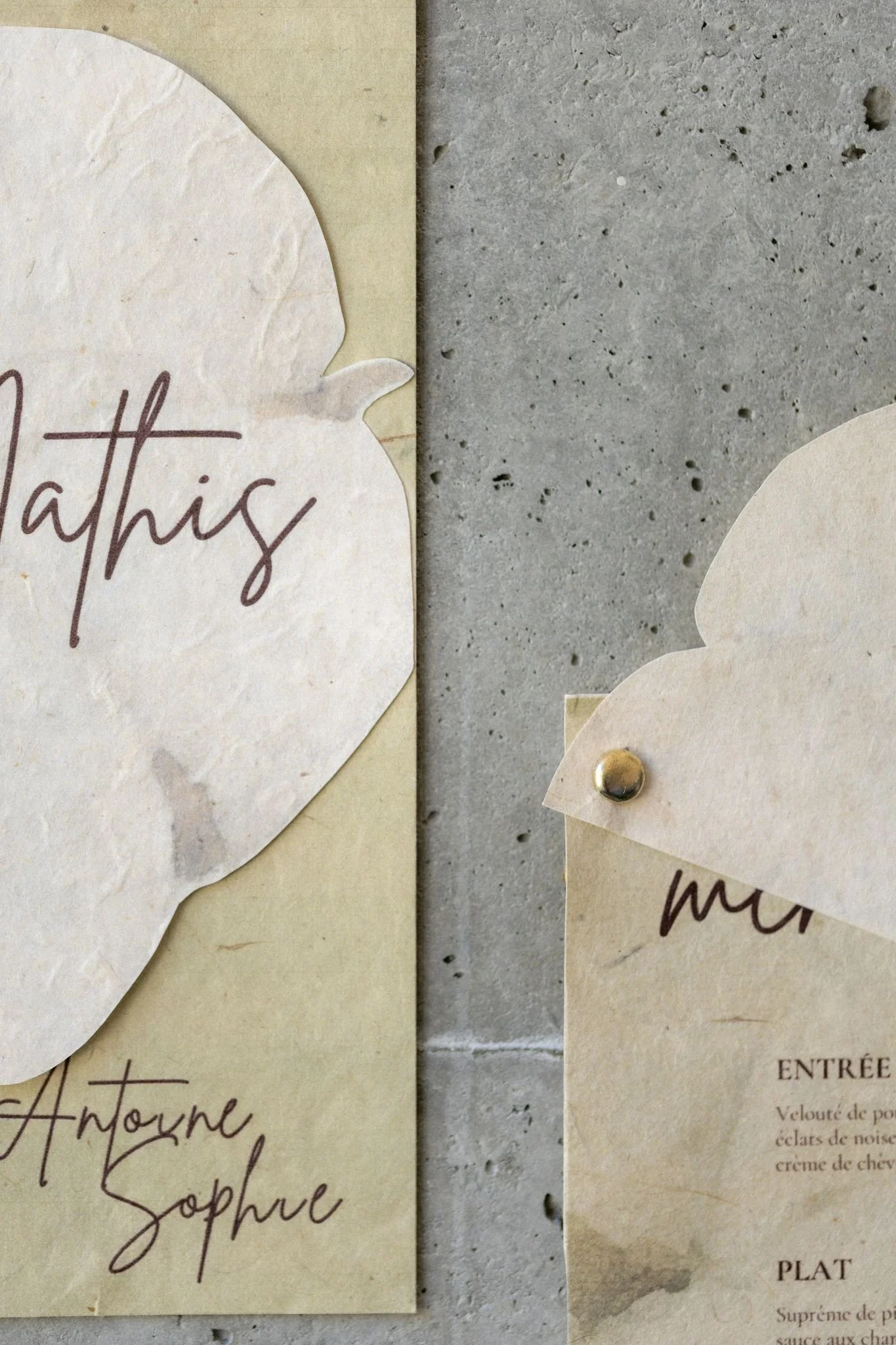 Une affiche en papier déchirée avec des écritures manuscrites en français, partiellement visible, fixée avec une punaise dorée sur un mur en béton. La partie visible montre des mots comme « Sophie » et « Antoine ».