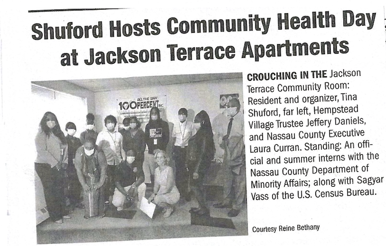 Group of people, some wearing masks, standing and kneeling in a room with a poster on the wall that says "ALL THE UP 100 PERCENT." This is a community health event at Jackson Terrace Apartments, with individuals including Tina Shuford, Nassau County Trustee Jeffery Daniels, Nassau County Executive Laura Curran, and interns from the Nassau County Department of Minority Affairs.
