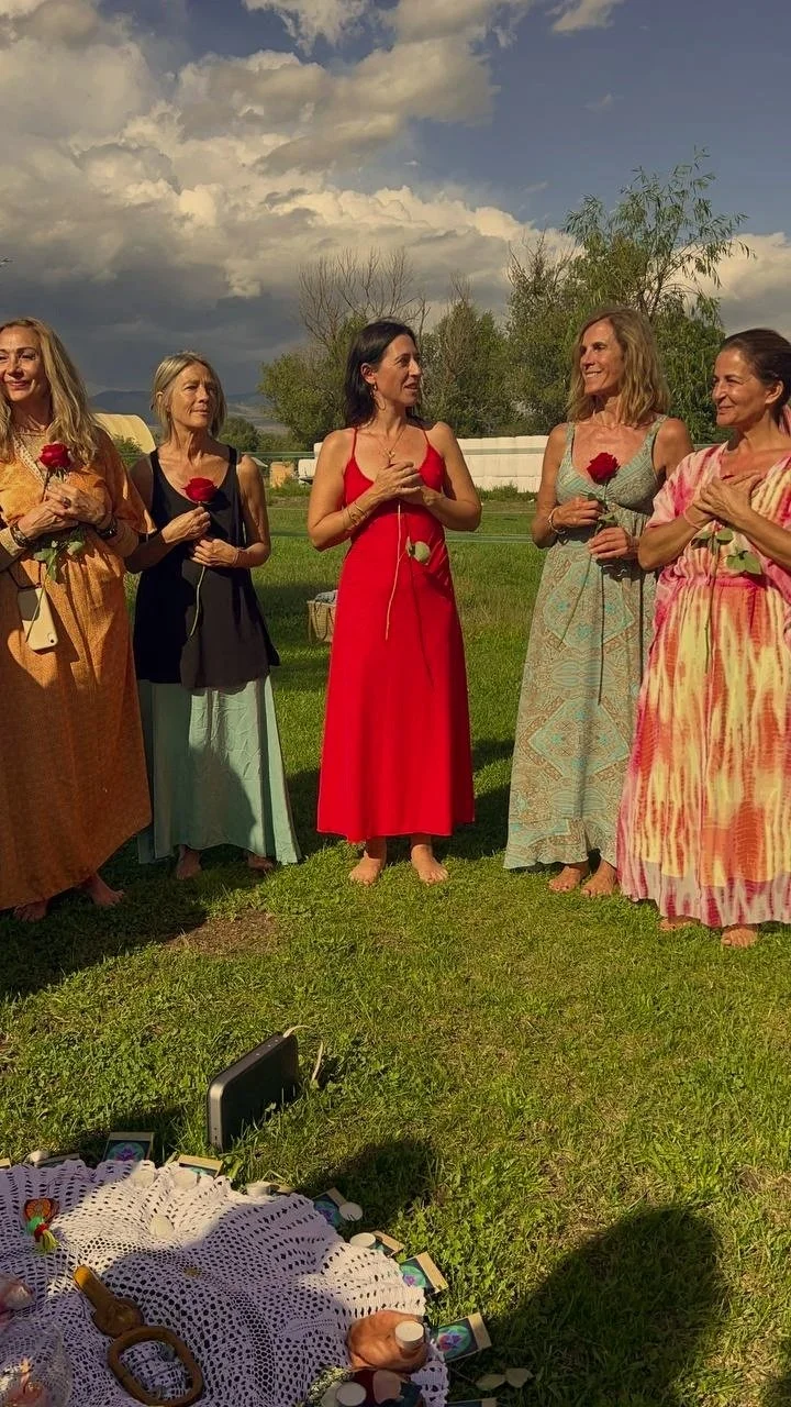 Grupo de mujeres en un campo, sosteniendo rosas rojas, en una ceremonia al aire libre.