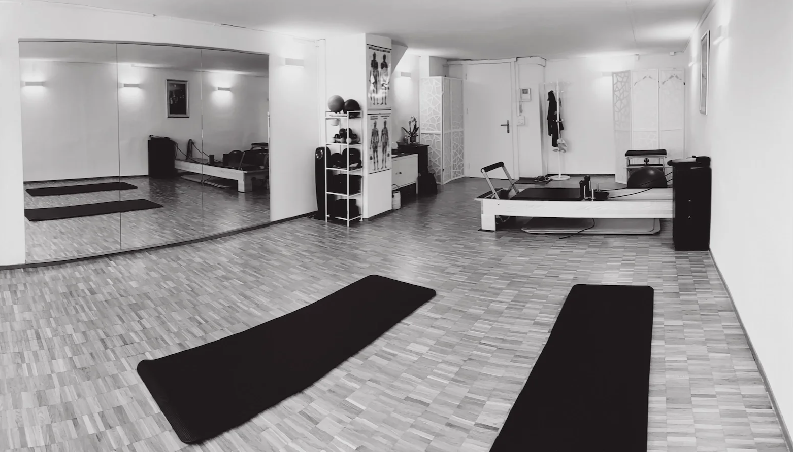 The ND Pilates studio with wooden flooring, black Pilates mats, a mirrored wall, and various exercise equipment, including medicine balls, a reformer machine, and a stability ball.