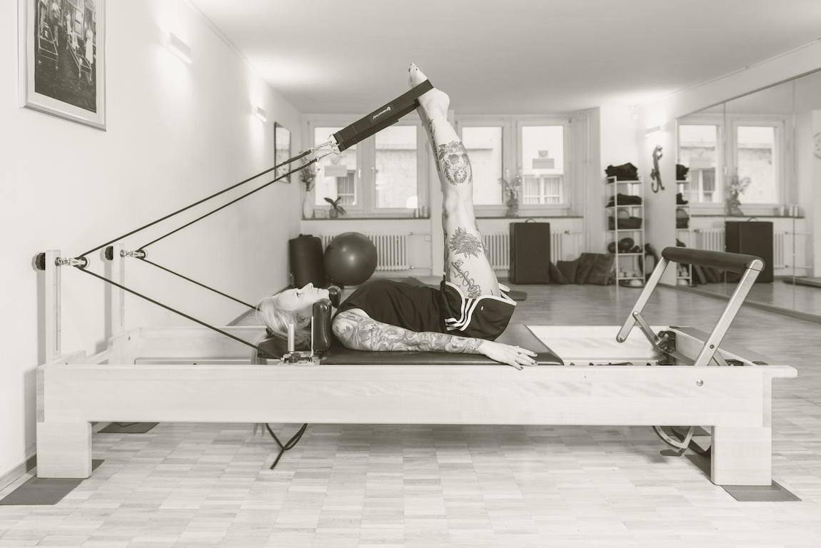 Tattooed woman using Pilates Reformer.webp