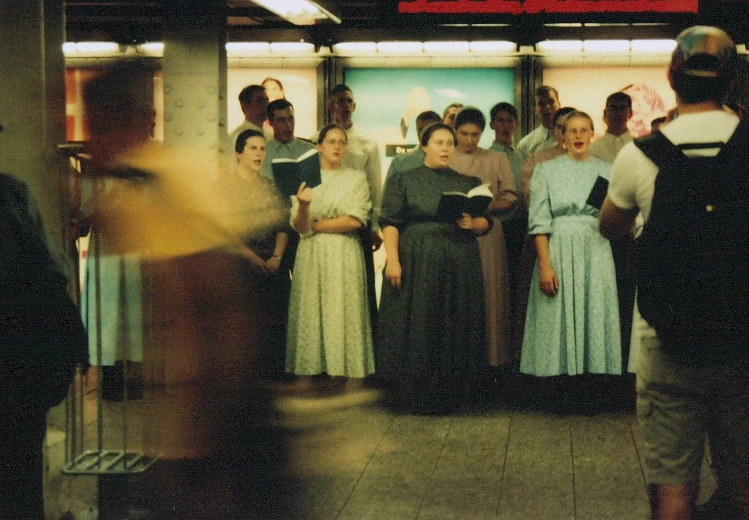 Eine Gruppe von Menschen singt in einem U-Bahnhof, einige halten Gesangsbücher in den Händen.