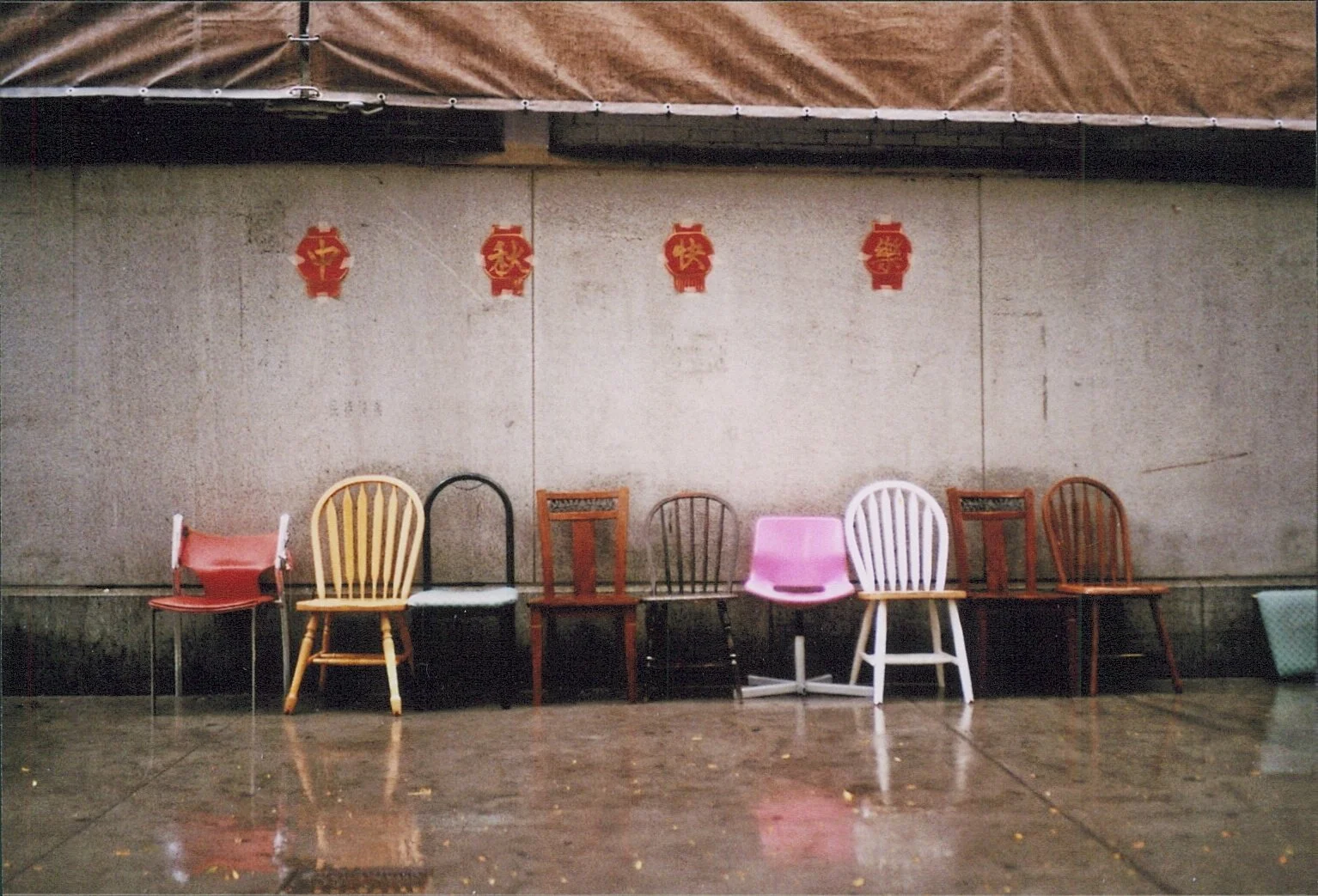 Verschiedene Stühle in einer Reihe vor einer grauen Wand mit roten chinesischen Dekorationen