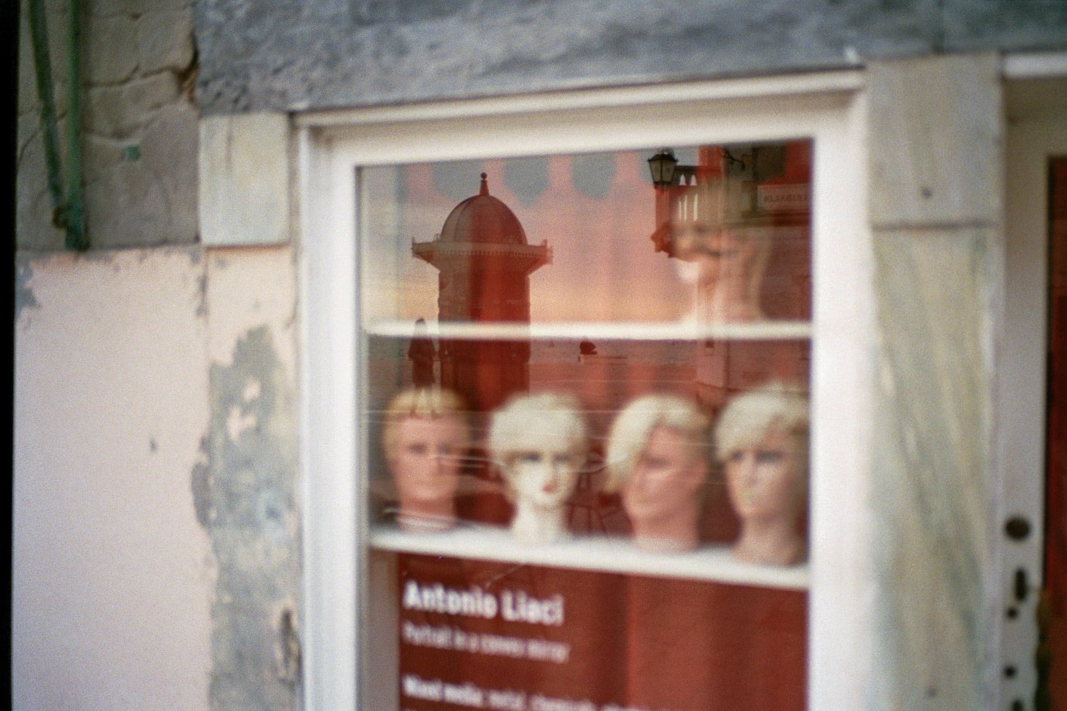 Reflexion eines historischen Turmgebäudes im Fenster eines Gebäudes mit Porträts auf der Innenseite