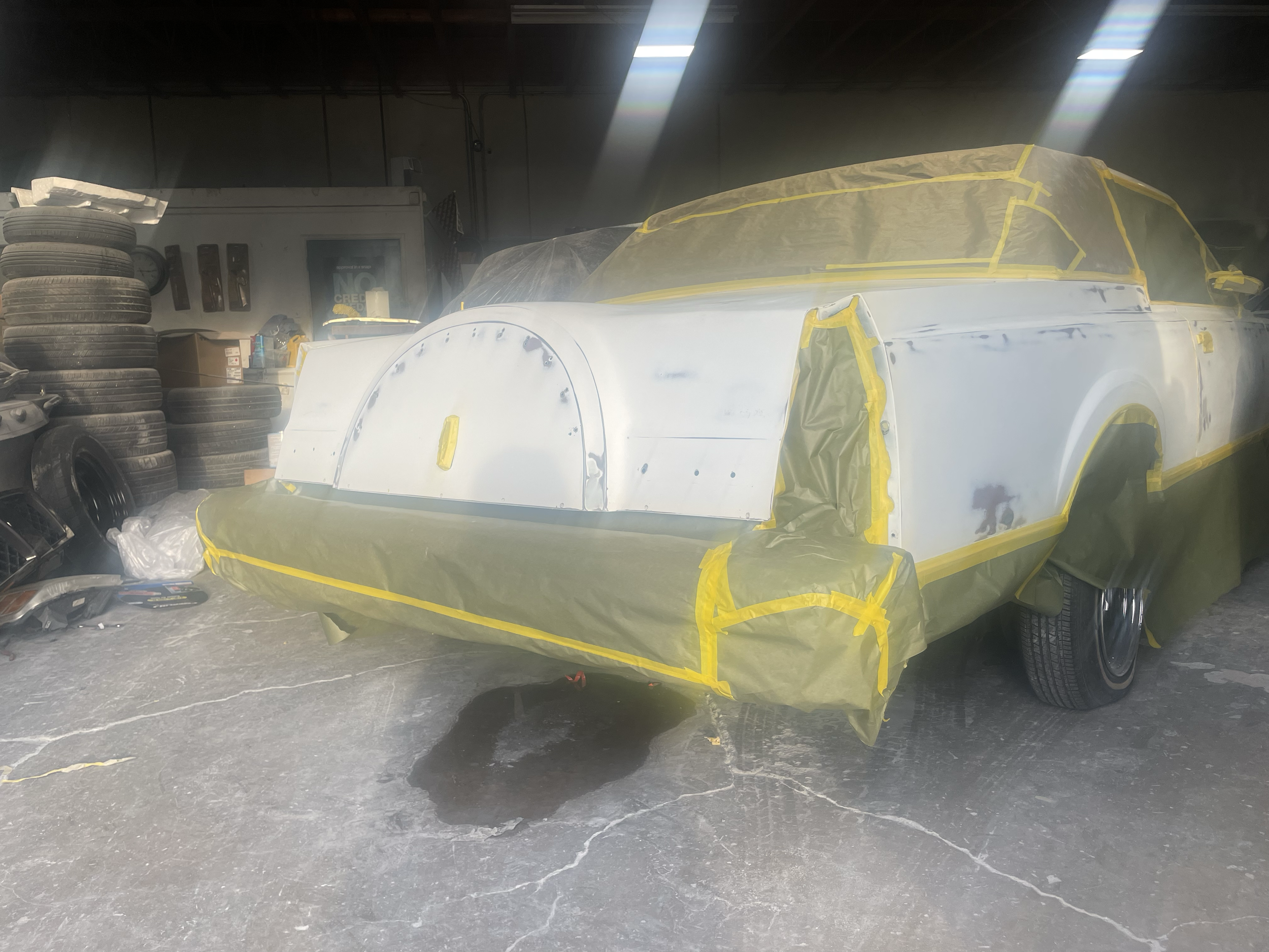 A car undergoing automotive bodywork repair in a workshop, covered with protective masking tape and plastic sheeting.