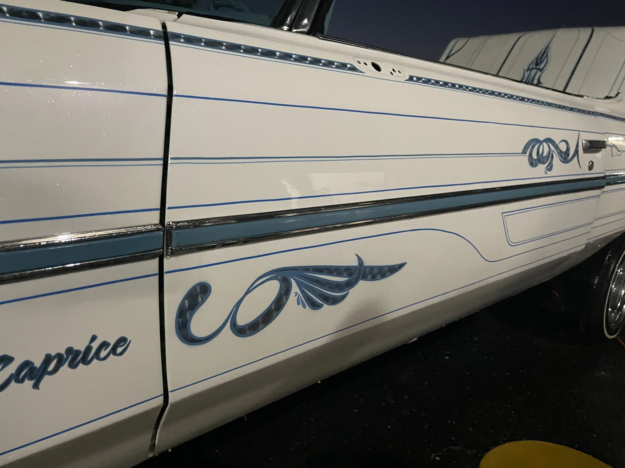 A vintage white car with blue pinstripes and decorative designs, parked outdoors at night.