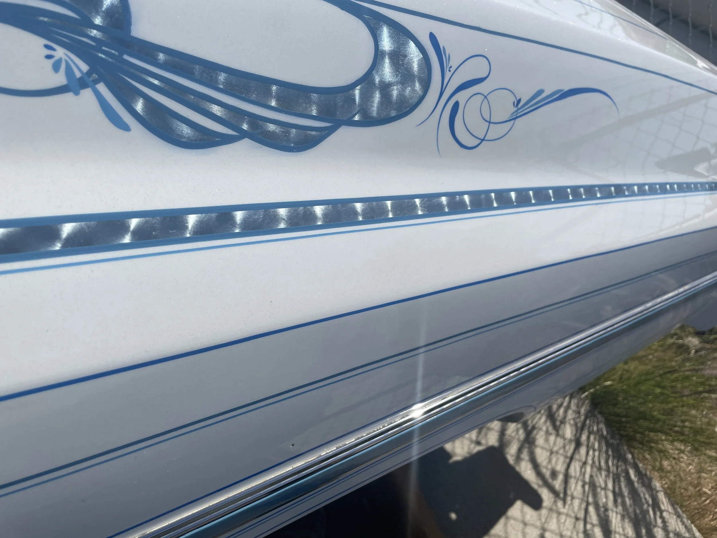 Close-up of a white surface with blue decorative lines and patterns, possibly a painted or printed design on an object, with some reflections and shadows visible.