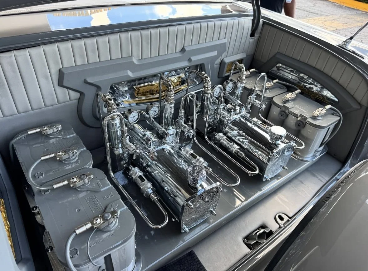Close-up of a vintage car's engine compartment with intricately designed metallic engine components and gauges.