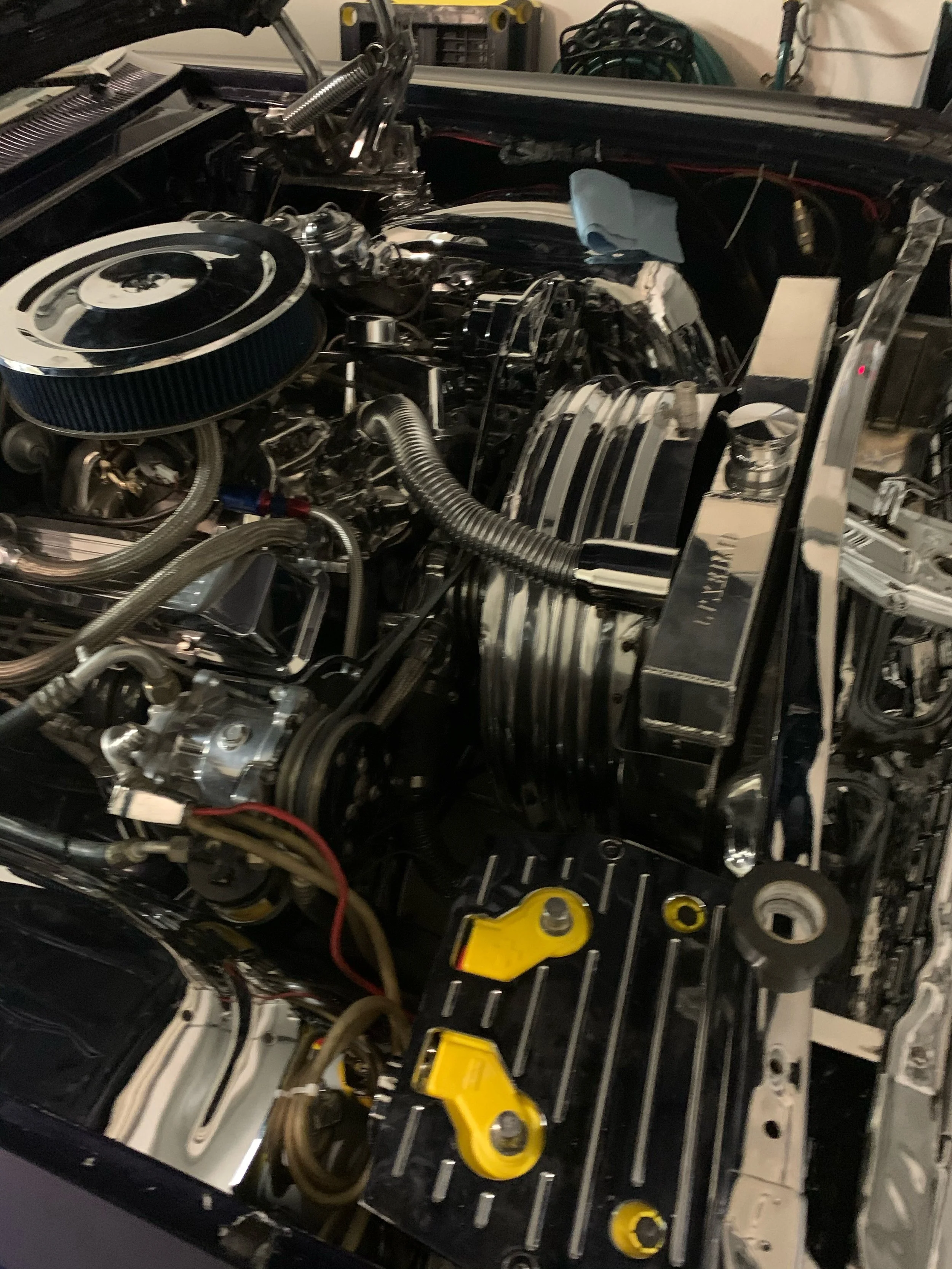 An opened car hood showing an engine with various metallic components, hoses, wires, and tools around.