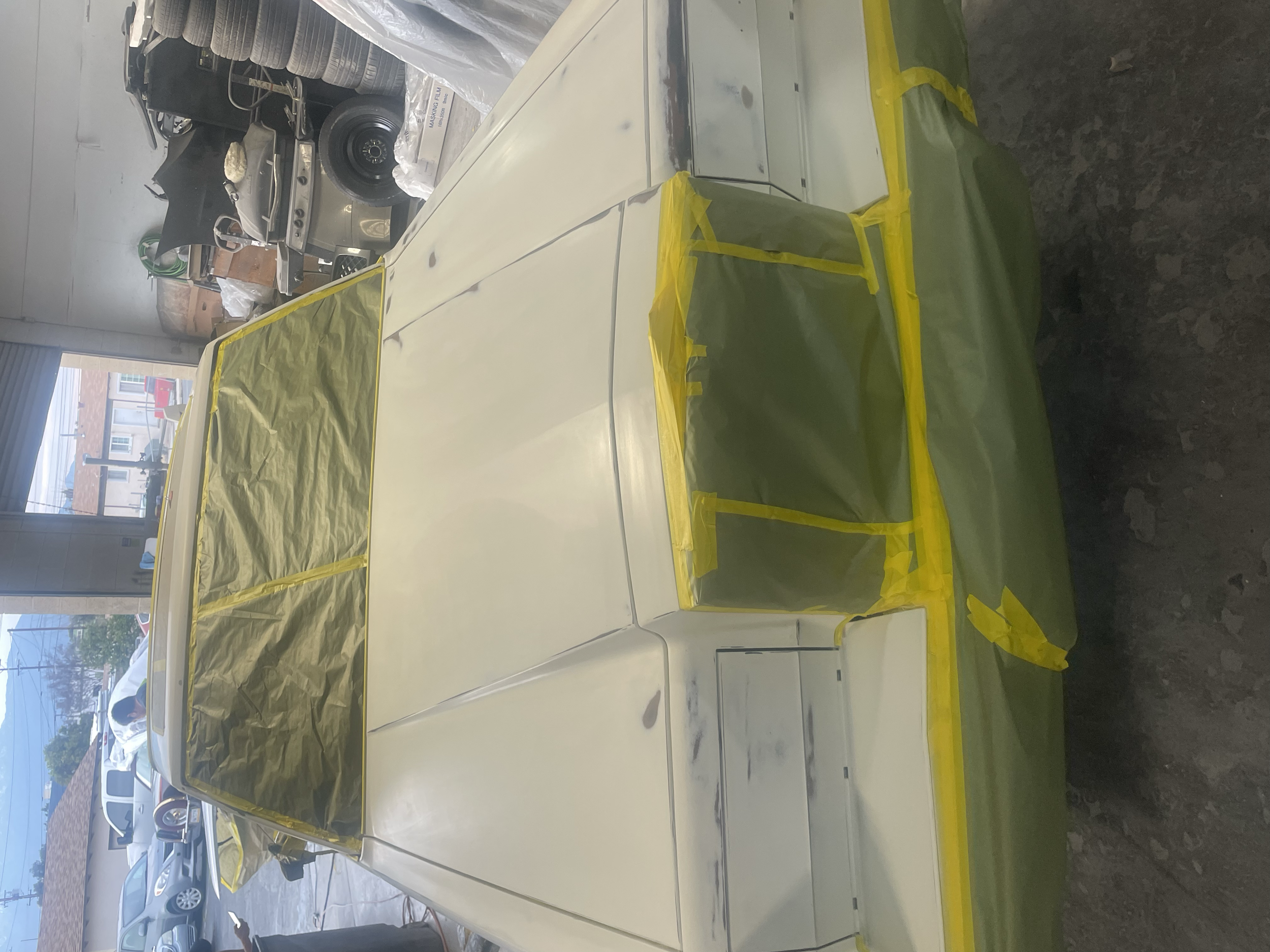 White appliance being spray painted with yellow masking tape and plastic coverings in a workshop.