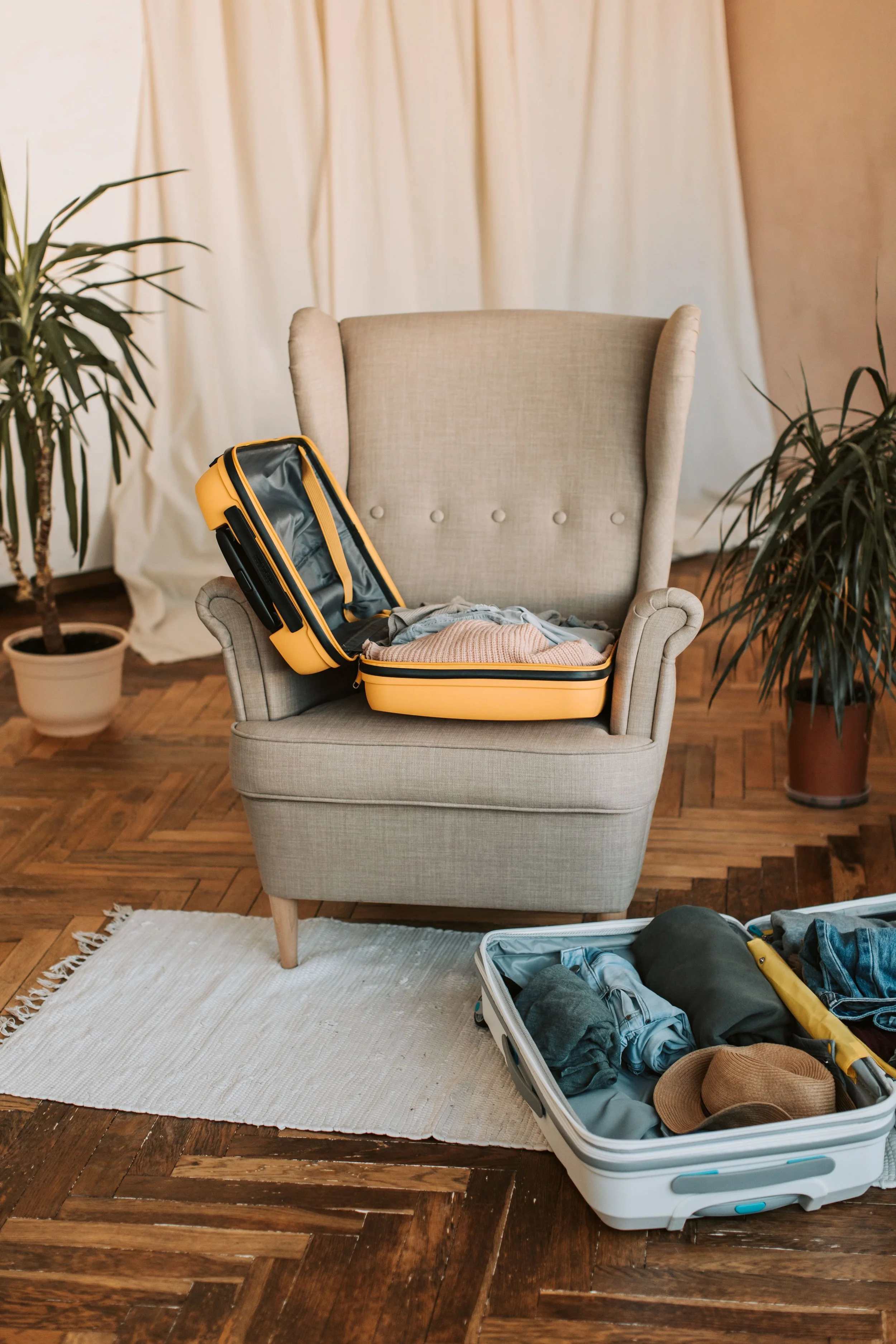Une pièce avec une chaise beige, des valises sont en cours de préparation pour des vacances en famille avec des enfants et des bébés, les valises sont trop chargées